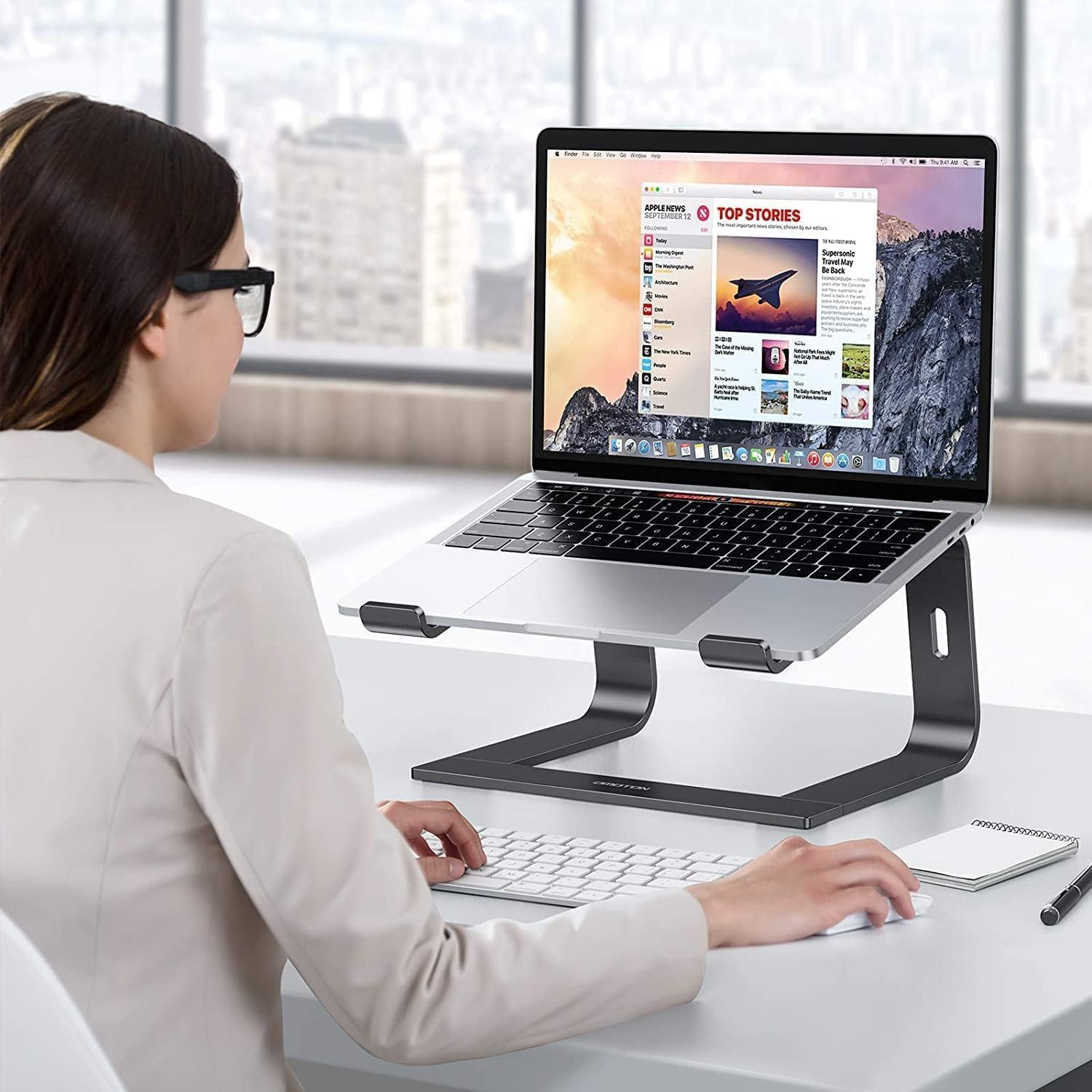 Frau mit Brille am Schreibtisch, die einen Laptop auf einem Ständer benutzt.