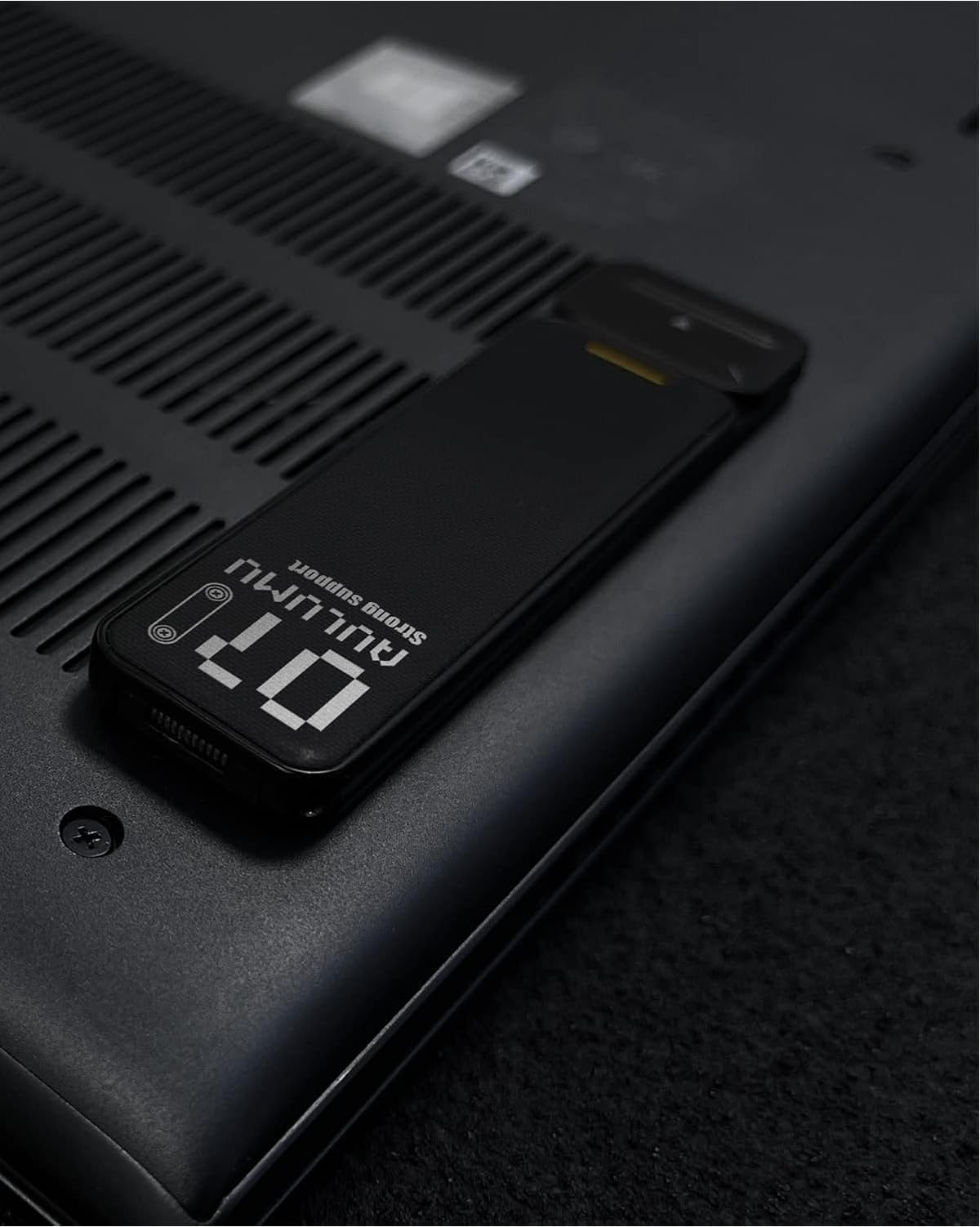 Ein schwarzer USB-Stick mit der Aufschrift „Strong Support“ liegt auf der Unterseite eines Laptops.