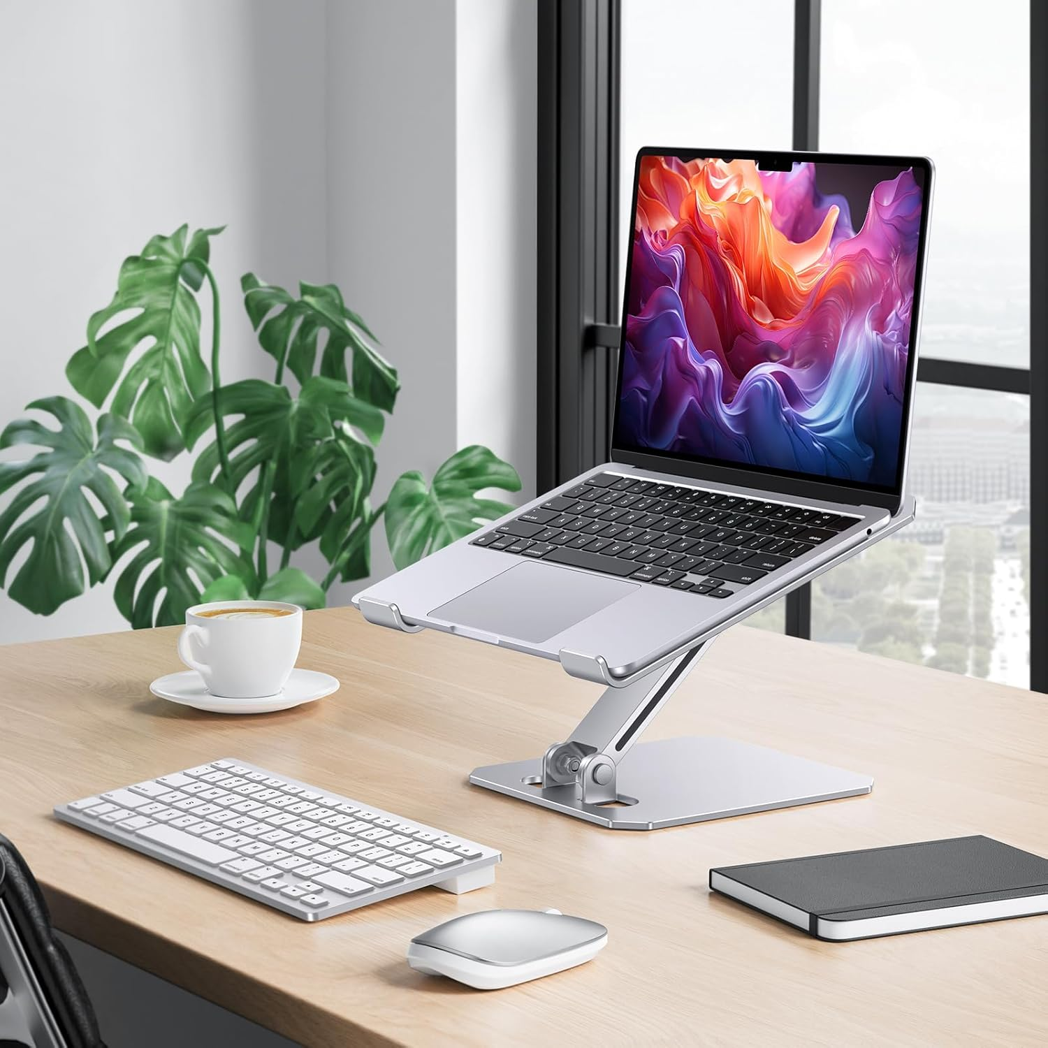 Ein Laptop auf einem Ständer, mit Tastatur, Maus, Kaffeetasse und Pflanze auf einem Holztisch.