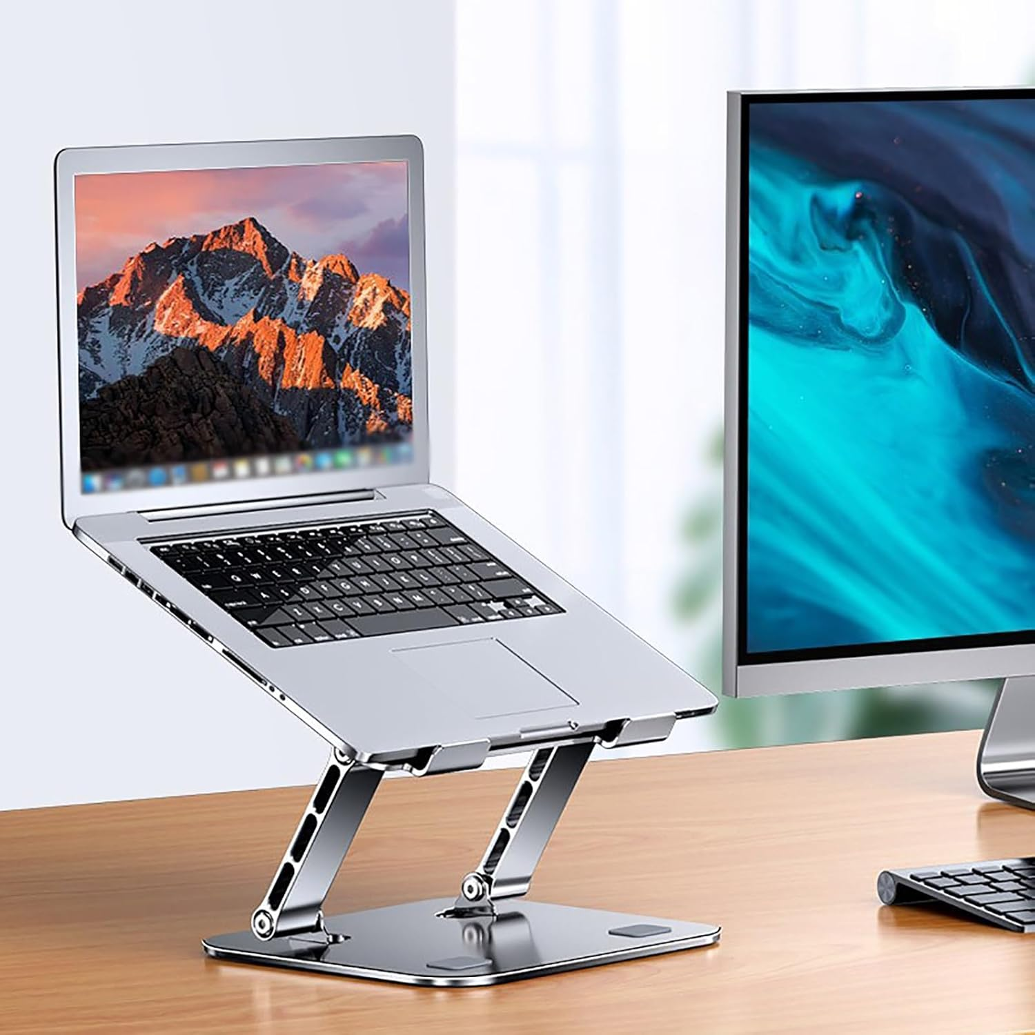 Ein silberner Laptop auf einem Ständer steht vor einem Monitor auf einem Holztisch.