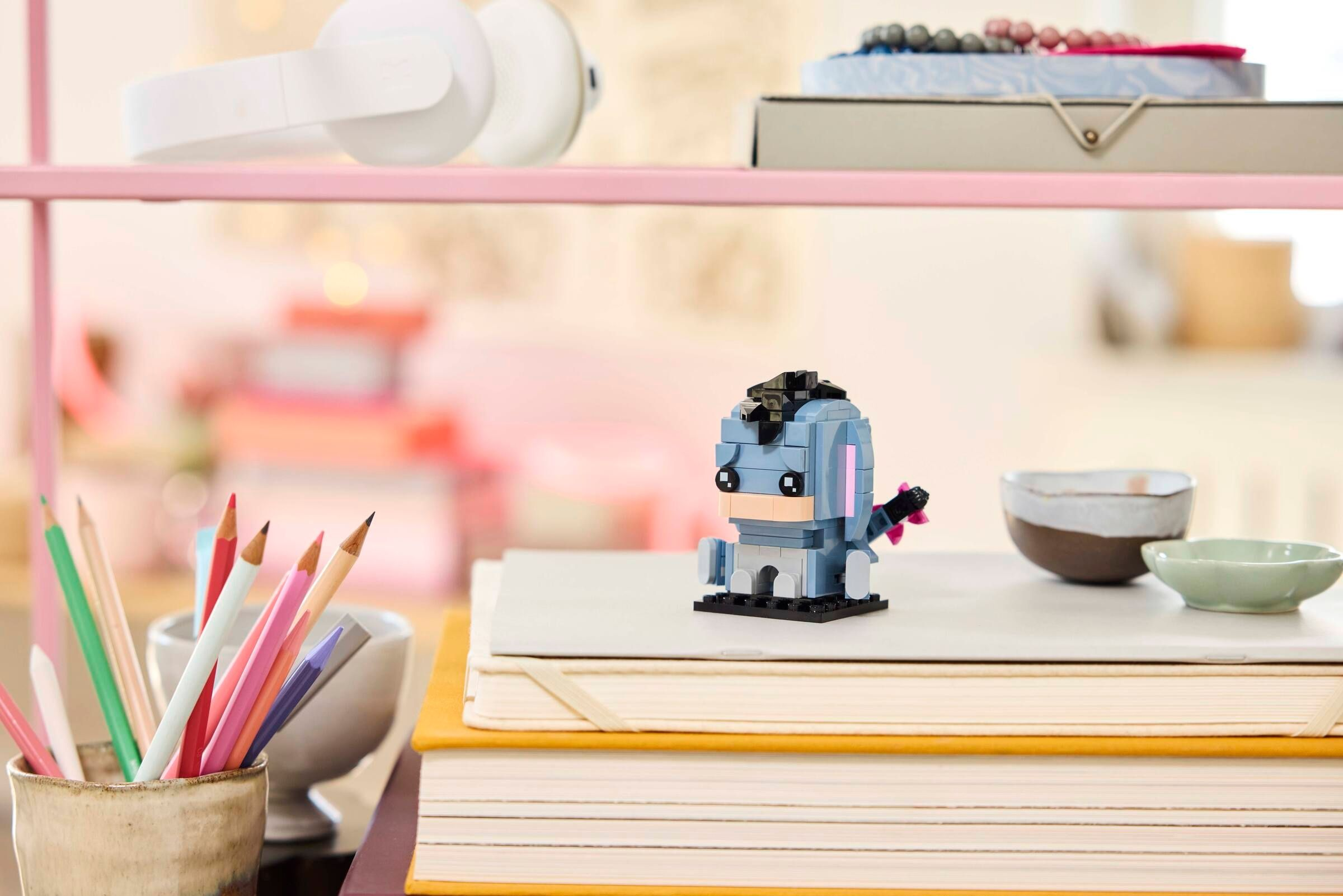 Bir LEGO Eeyore, kalemlerin ve kaselerin yanında kitapların üzerinde oturuyor.