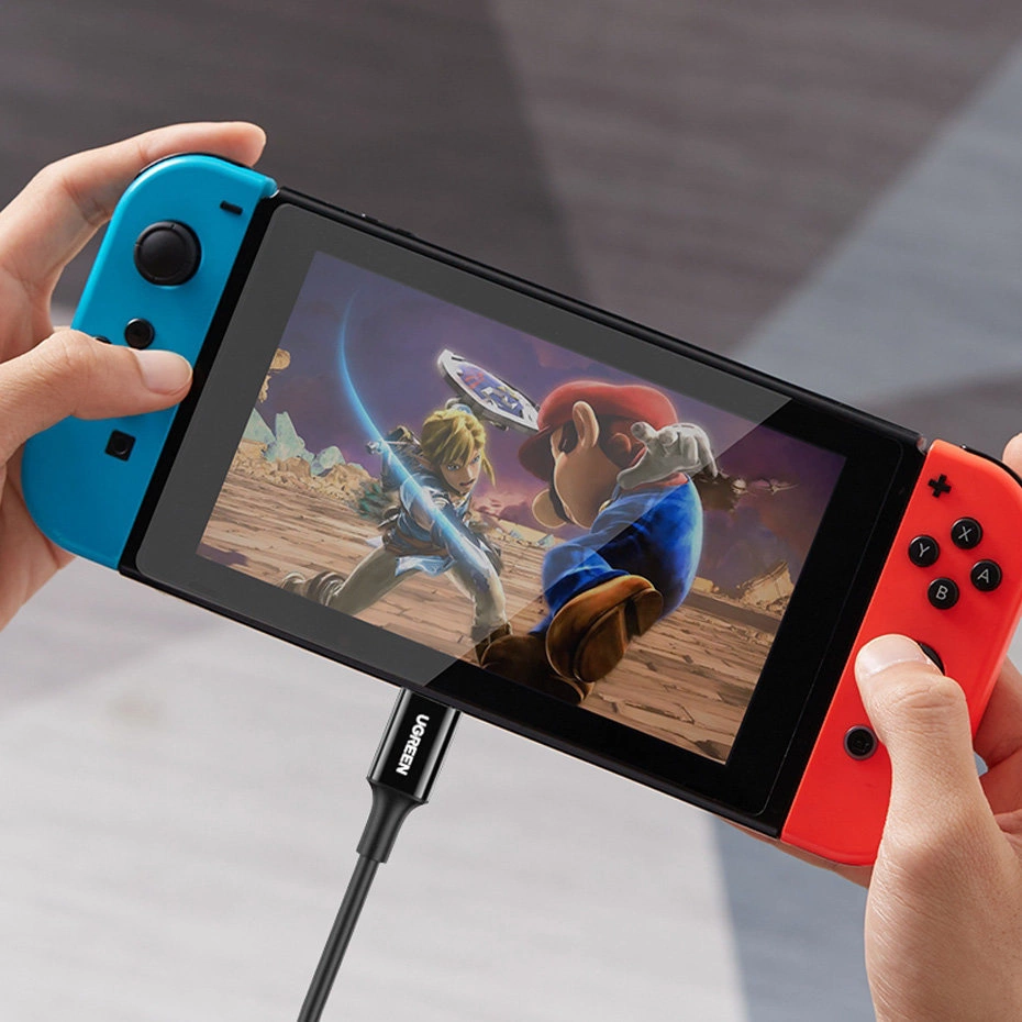 Osoba gra na Nintendo Switch z Linkiem i Mario na ekranie, ładuje przez kabel USB-C.
