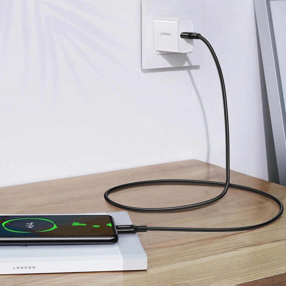 Czarny kabel ładujący łączy smartfon z białym adapterem w gniazdku ściennym.