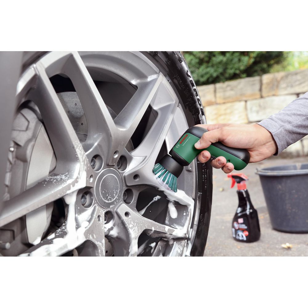 Eine Hand benutzt eine grüne Bürste, um ein Auto-Rad mit Schaum zu reinigen.