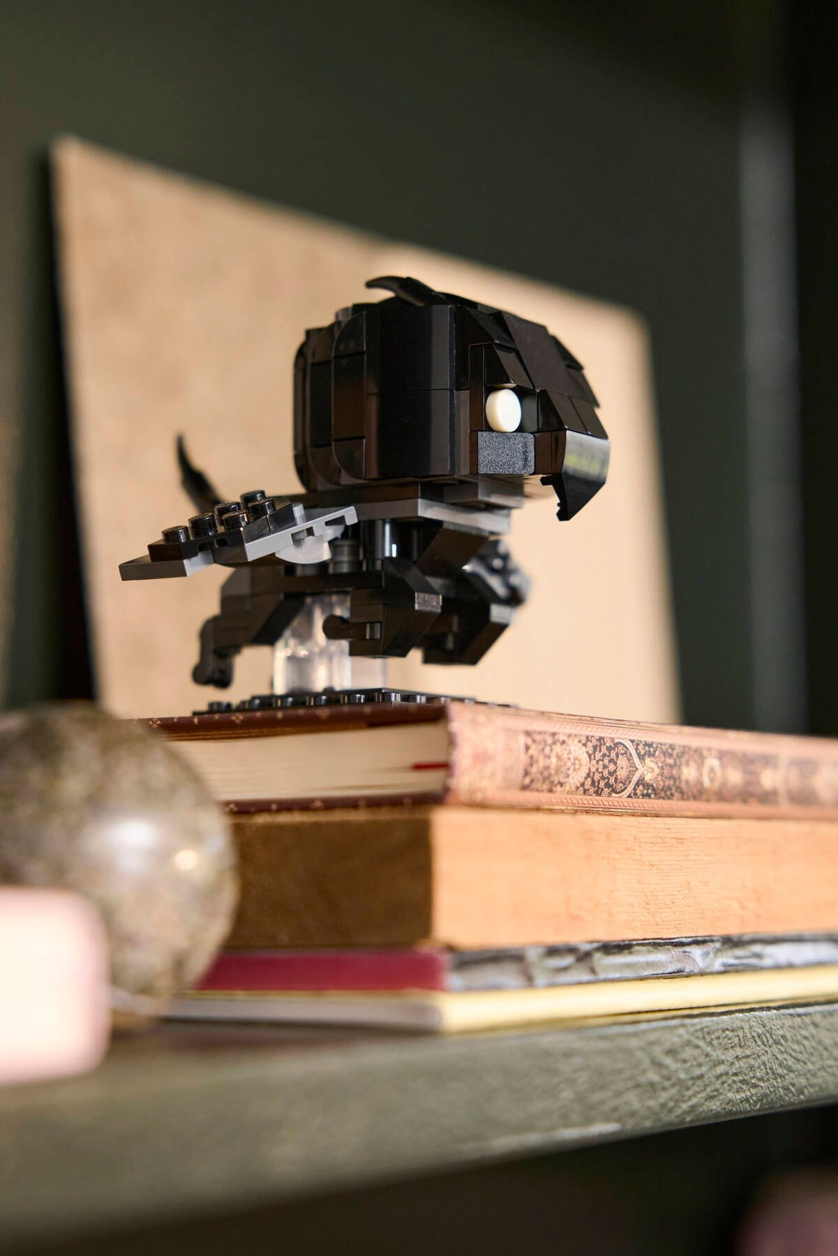 Beyaz gözlü siyah Lego figürü kitapların üzerinde oturuyor.