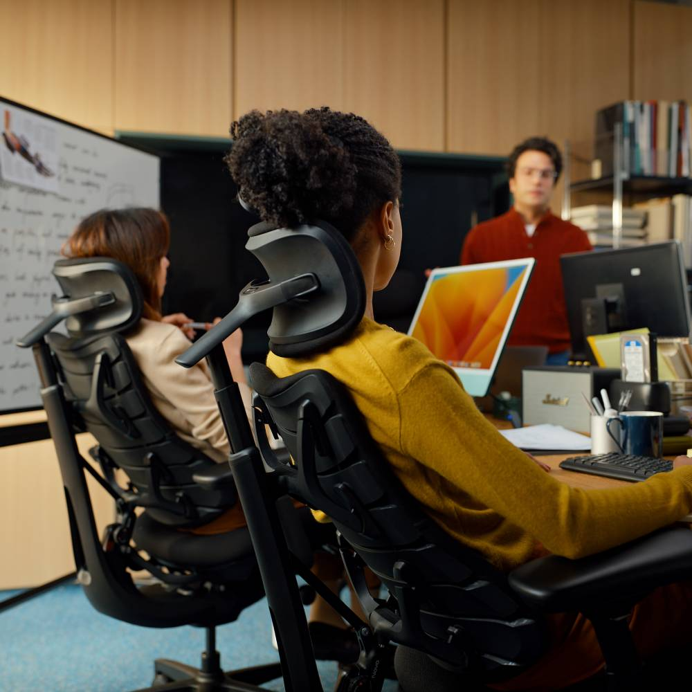 Bureau avec personnel sur des ordinateurs, femme en pull jaune sur une chaise de bureau.
