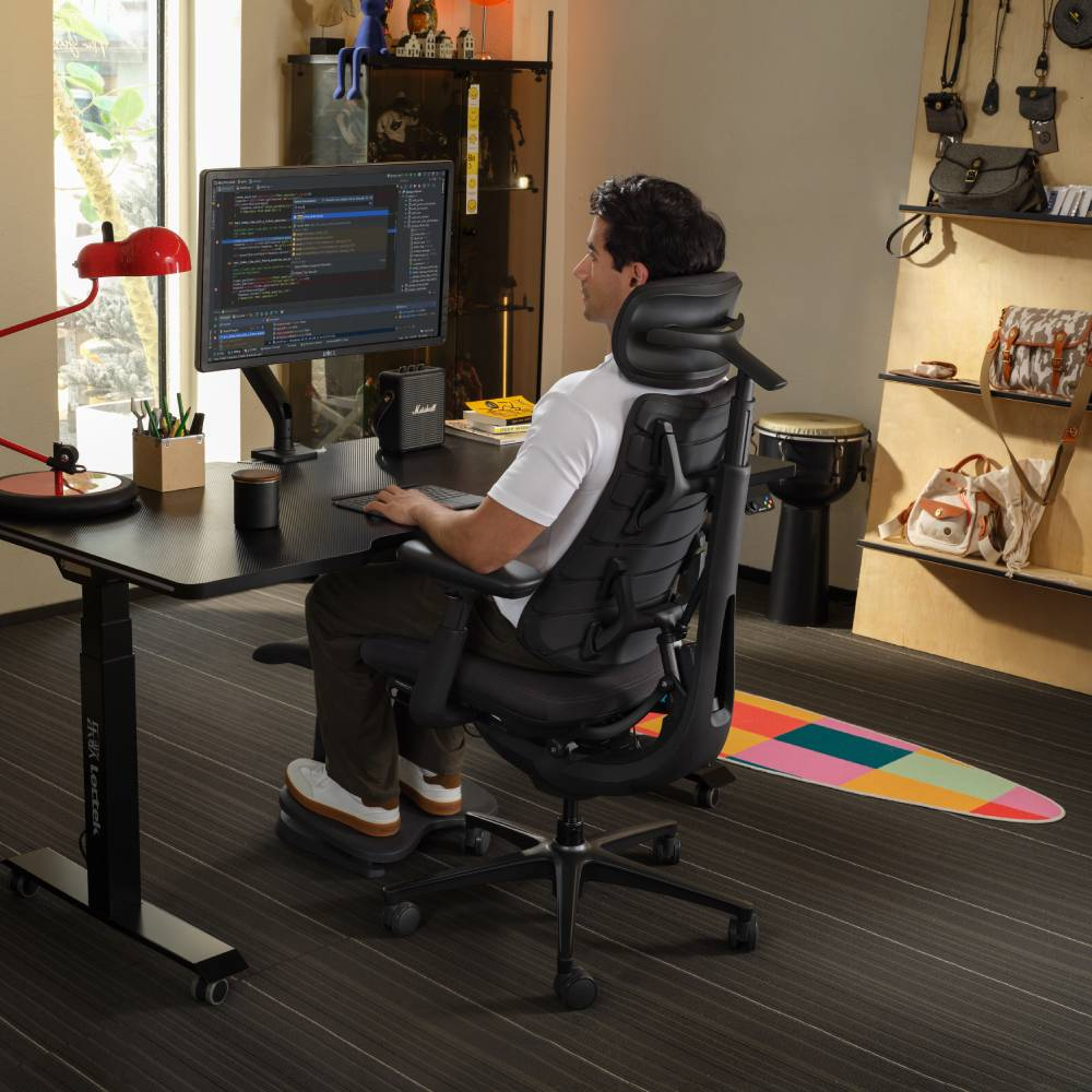 Un homme est assis à un bureau, travaillant sur un ordinateur. Une chaise de bureau avec appui-tête.