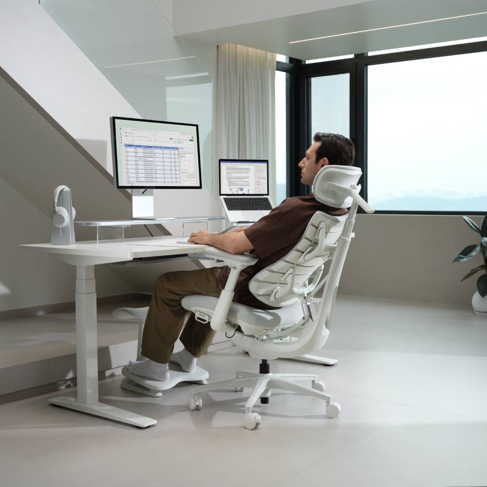 Homme assis à un bureau avec deux moniteurs et un ordinateur portable. Chaise de bureau moderne.