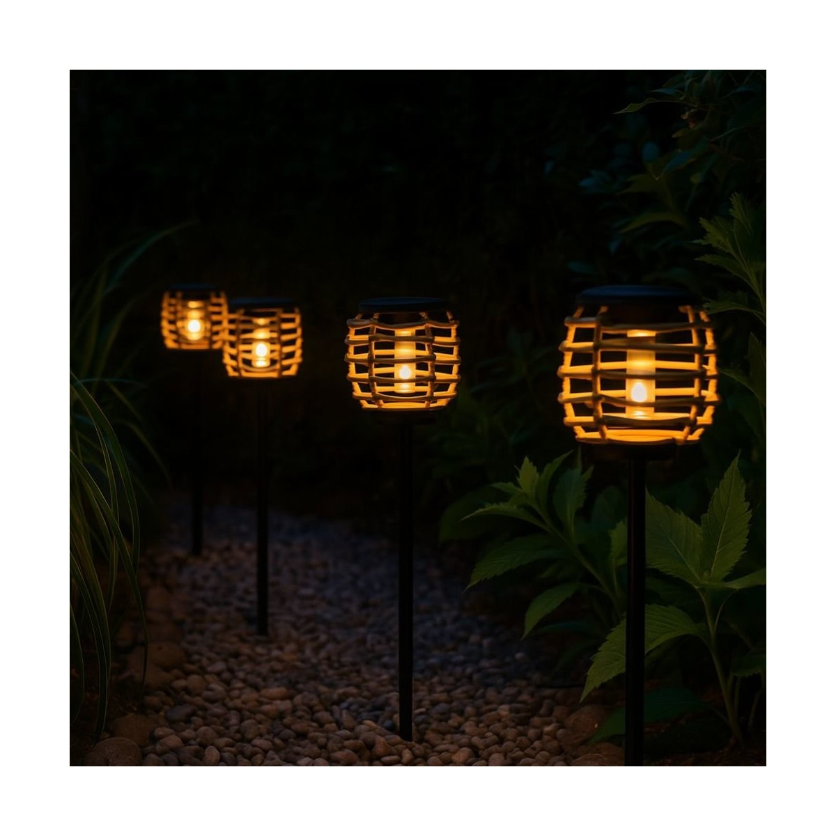 Vier verlichte rotan design solar lampen staan 's nachts langs een grindtuinpad.