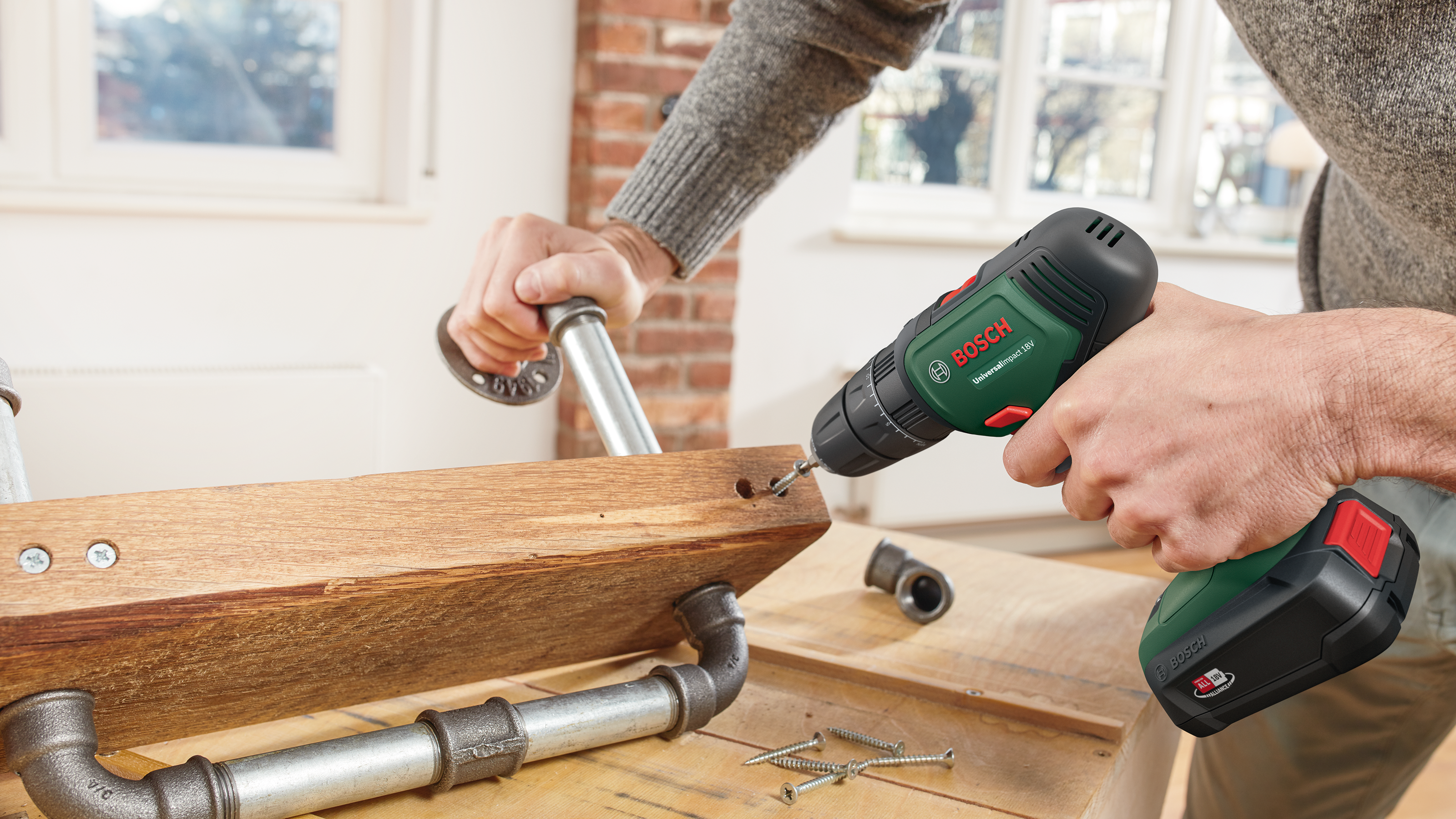 Un uomo usa un trapano Bosch verde per avvitare un raccordo a un'asse di legno.