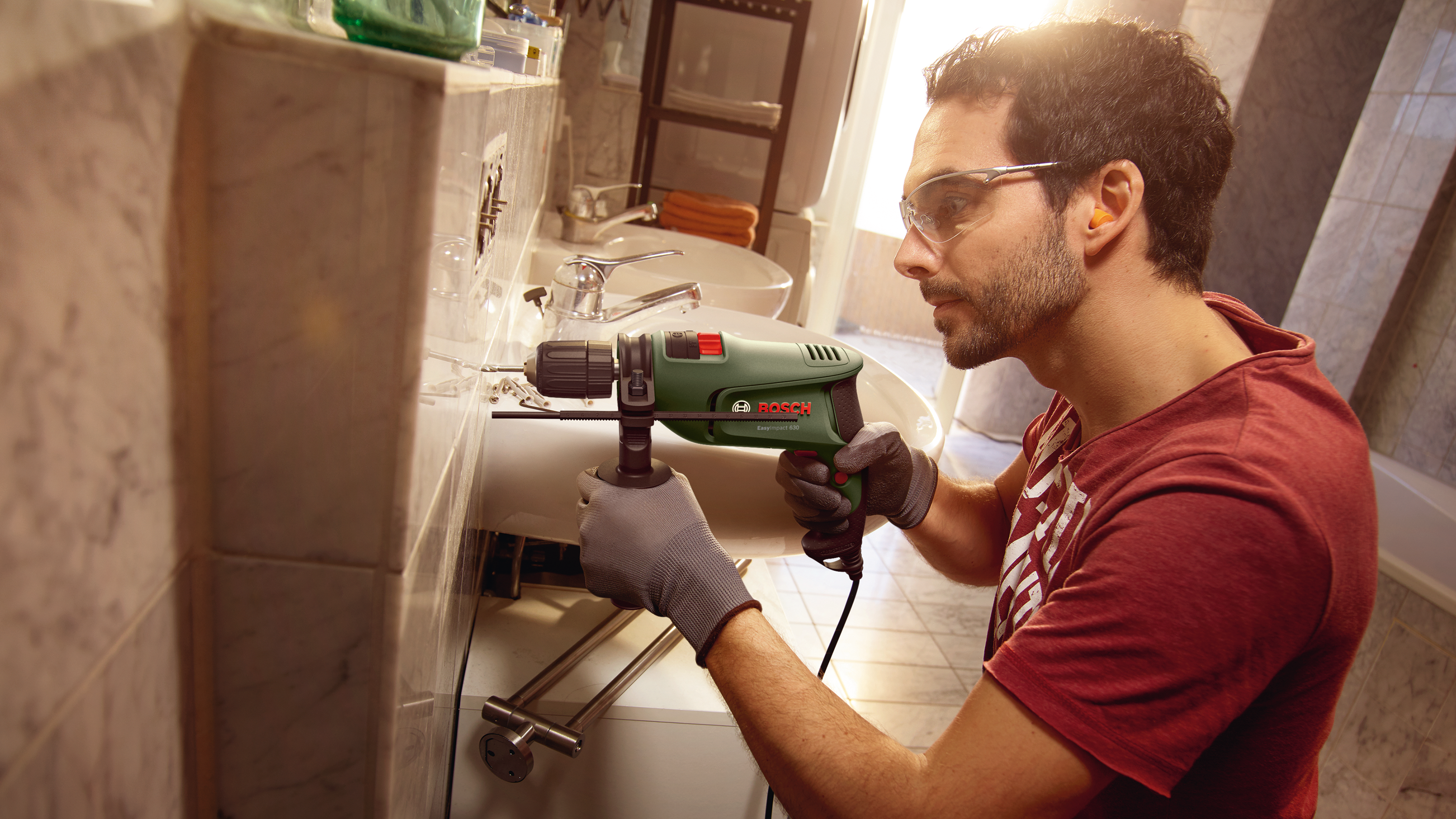Hombre con gafas de seguridad perfora un lavabo, llevando guantes.