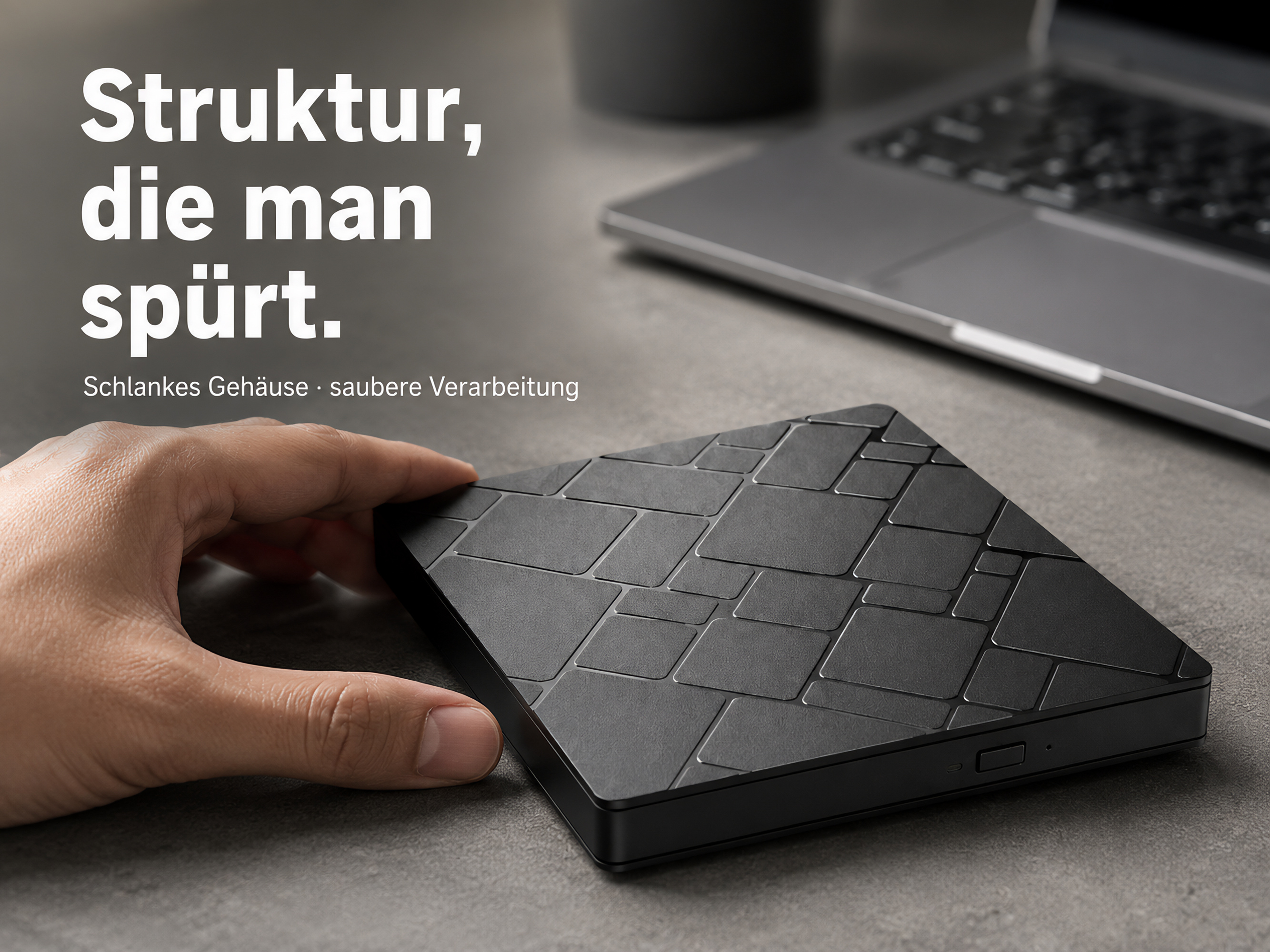 Schwarzes, texturiertes rechteckiges Gerät mit einer Laptop-Tastatur im Hintergrund.