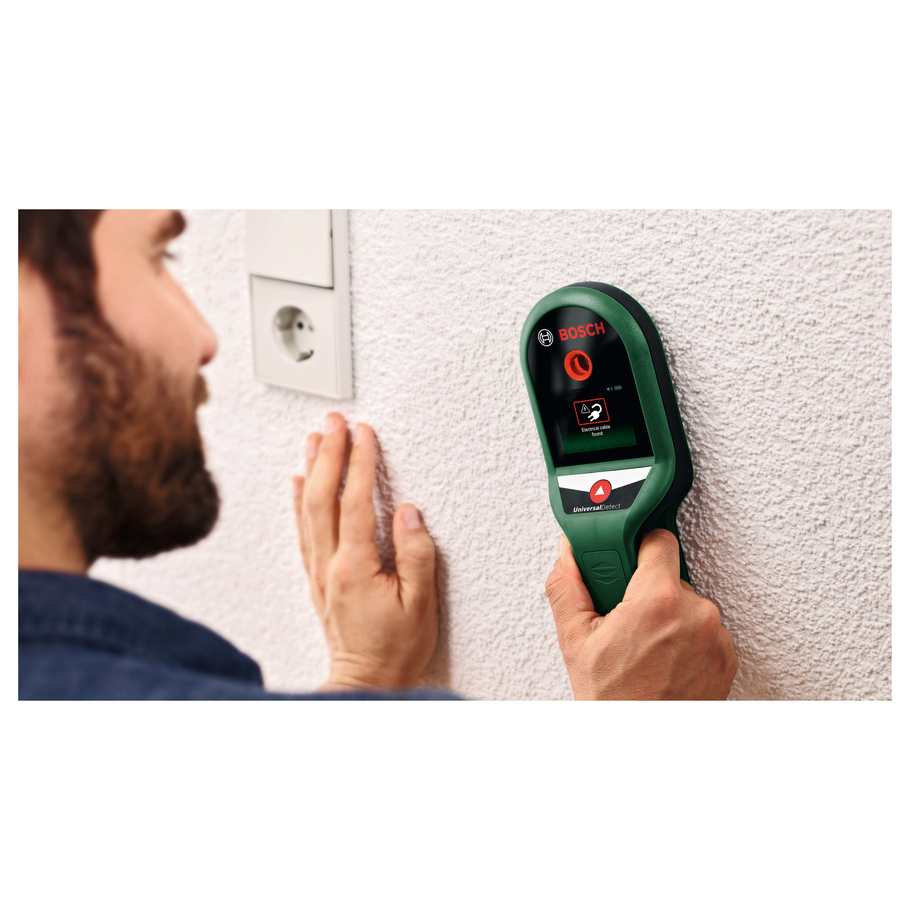 Ein Mann nutzt ein grünes Bosch Ortungsgerät an einer weißen Wand.