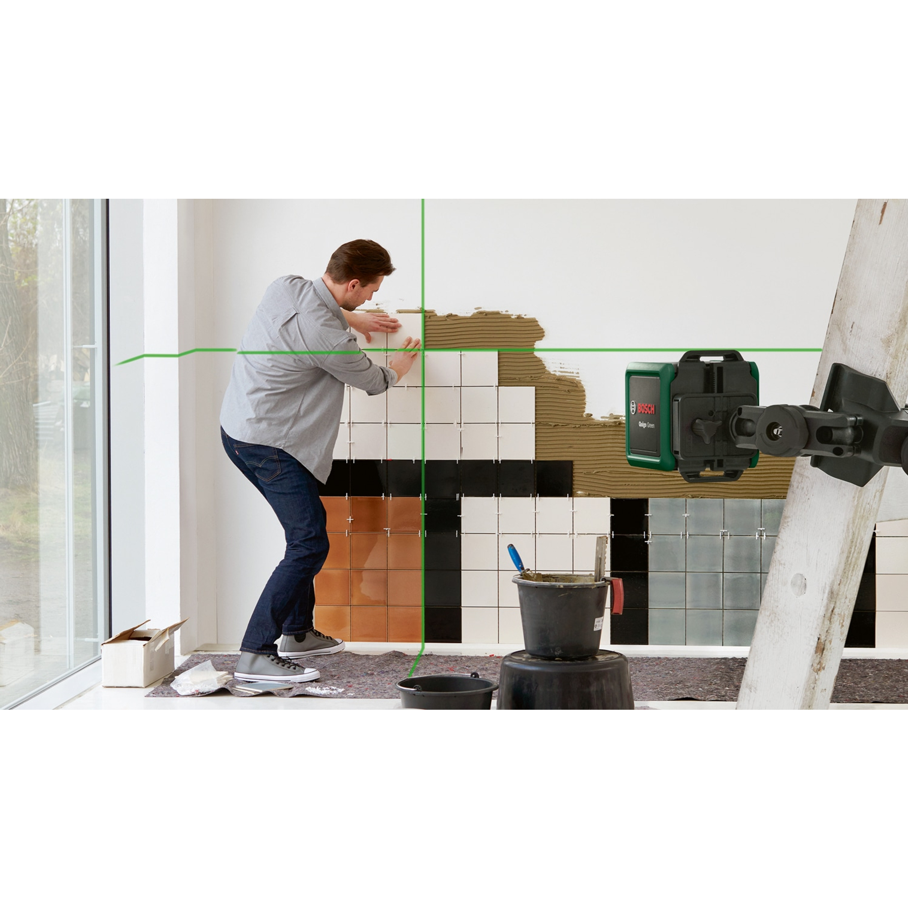 Ein Mann klebt Fliesen an eine Wand, angeleitet von einem grünen Laserlinien-Projektor.