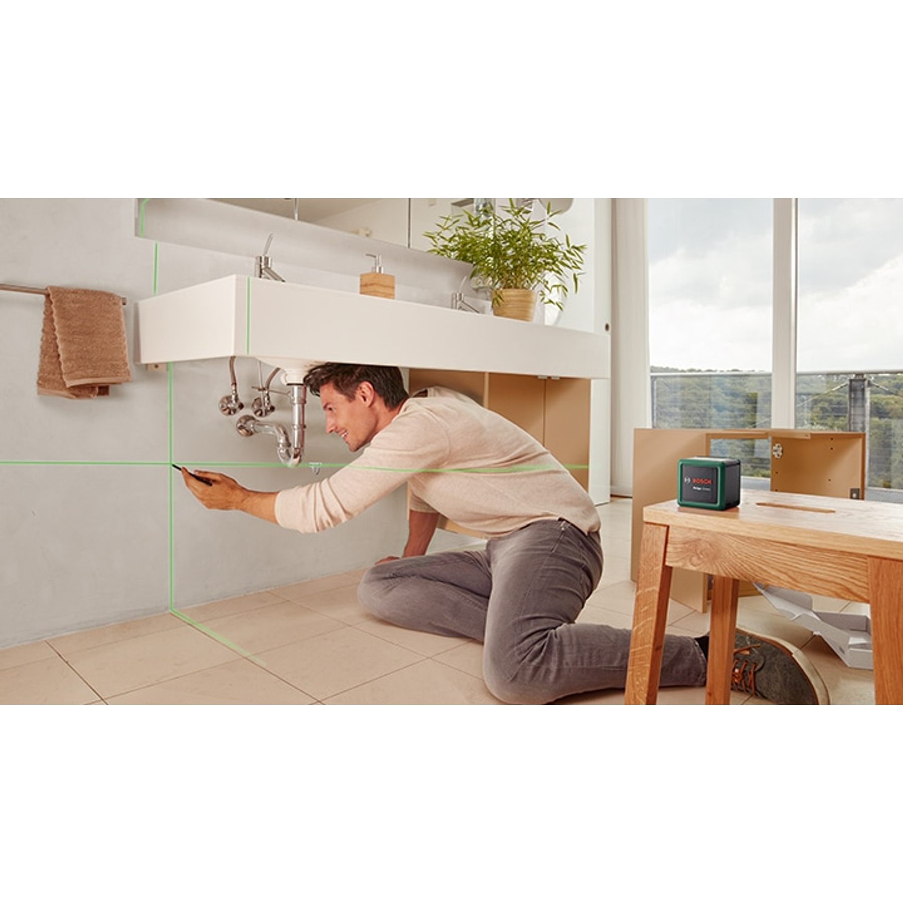 Ein Mann benutzt einen grünen Laser-Entfernungsmesser, um eine Badezimmerwand zu markieren.