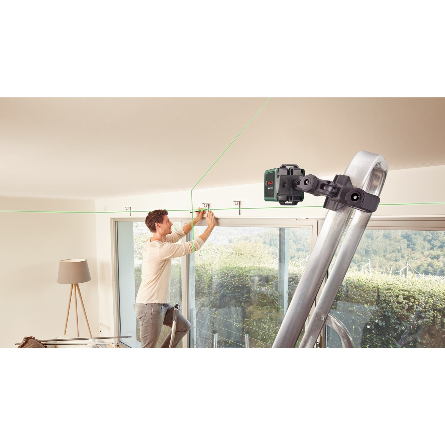 Ein Mann steht auf einer Leiter und nutzt einen grünen Laser, um Halterungen an einer Wand auszurichten.