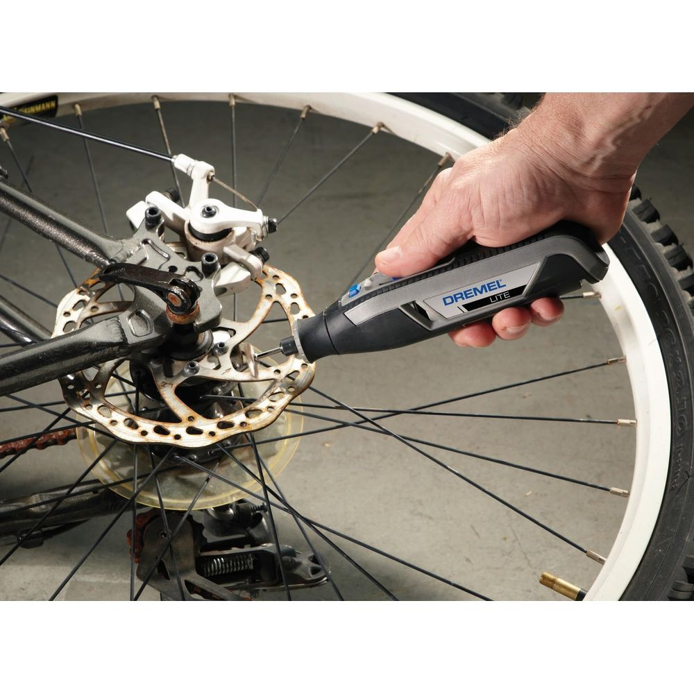 Eine Hand hält einen Dremel-Multifunktionswerkzeug, um die rostige Bremsscheibe eines Fahrrads zu bearbeiten.
