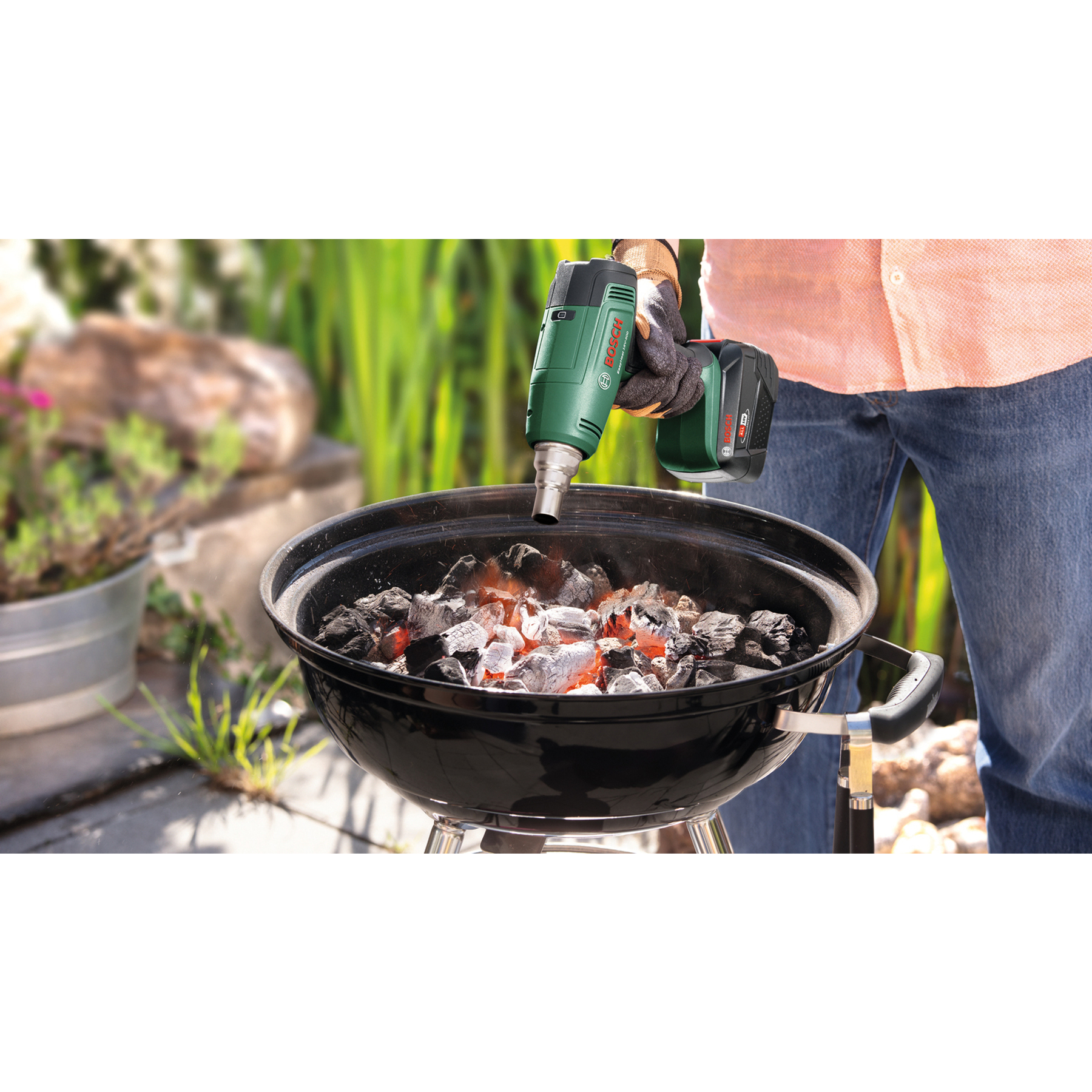 Eine Person benutzt eine grüne Akku-Heißluftpistole, um Holzkohle in einem Grill anzuzünden.