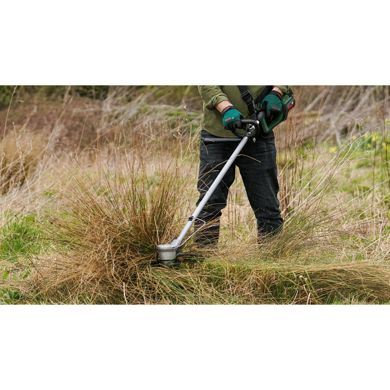 Person in grüner Jacke schneidet hohes Gras mit einem Freischneider.
