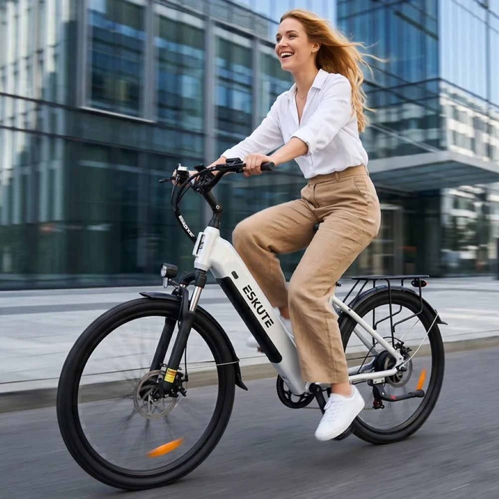 Una donna bionda sorridente guida una bicicletta elettrica Eskute bianca davanti a moderni uffici di vetro.