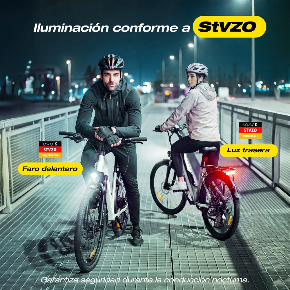 Dos ciclistas con casco montan en bicicleta eléctrica de noche por un puente con luces.