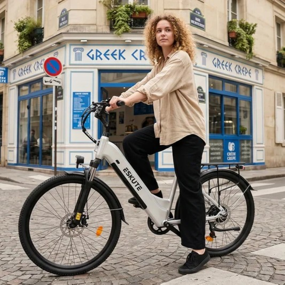 Una donna con capelli biondi ricci posa su una bici elettrica bianca davanti a un negozio a Parigi.