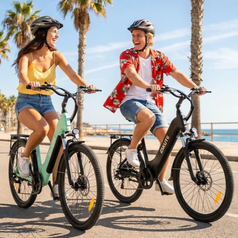 Una coppia felice guida e-bike su una strada sul mare fiancheggiata da palme.