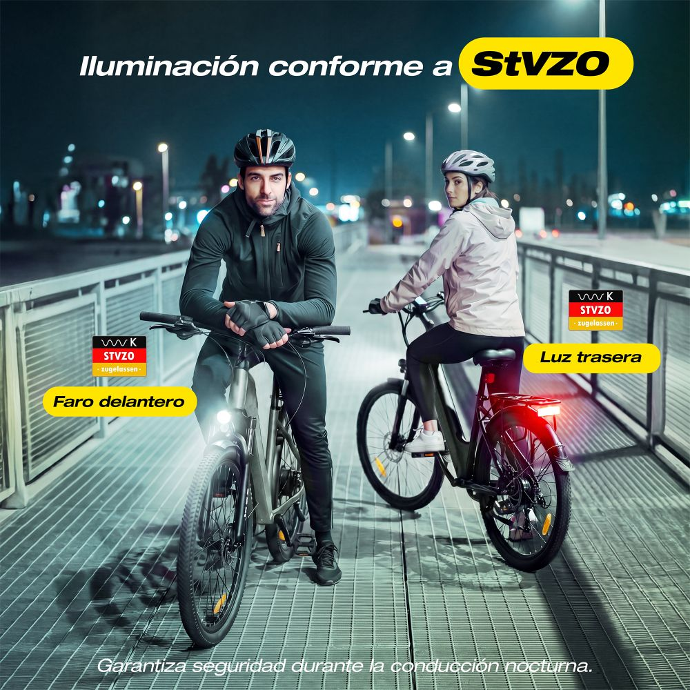 Un hombre y una mujer montan en bicicleta de noche en un puente metálico con luces.