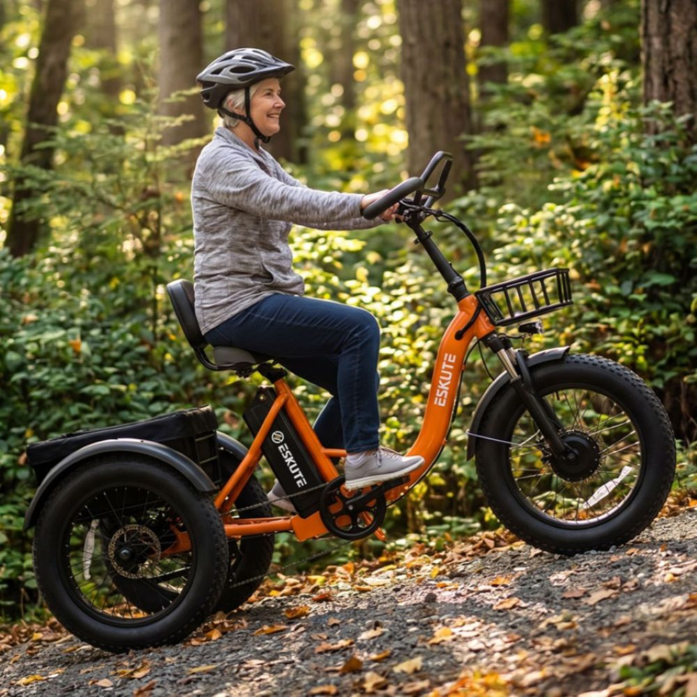 Una mujer mayor monta un triciclo eléctrico naranja en un sendero arbolado cubierto de hojas.