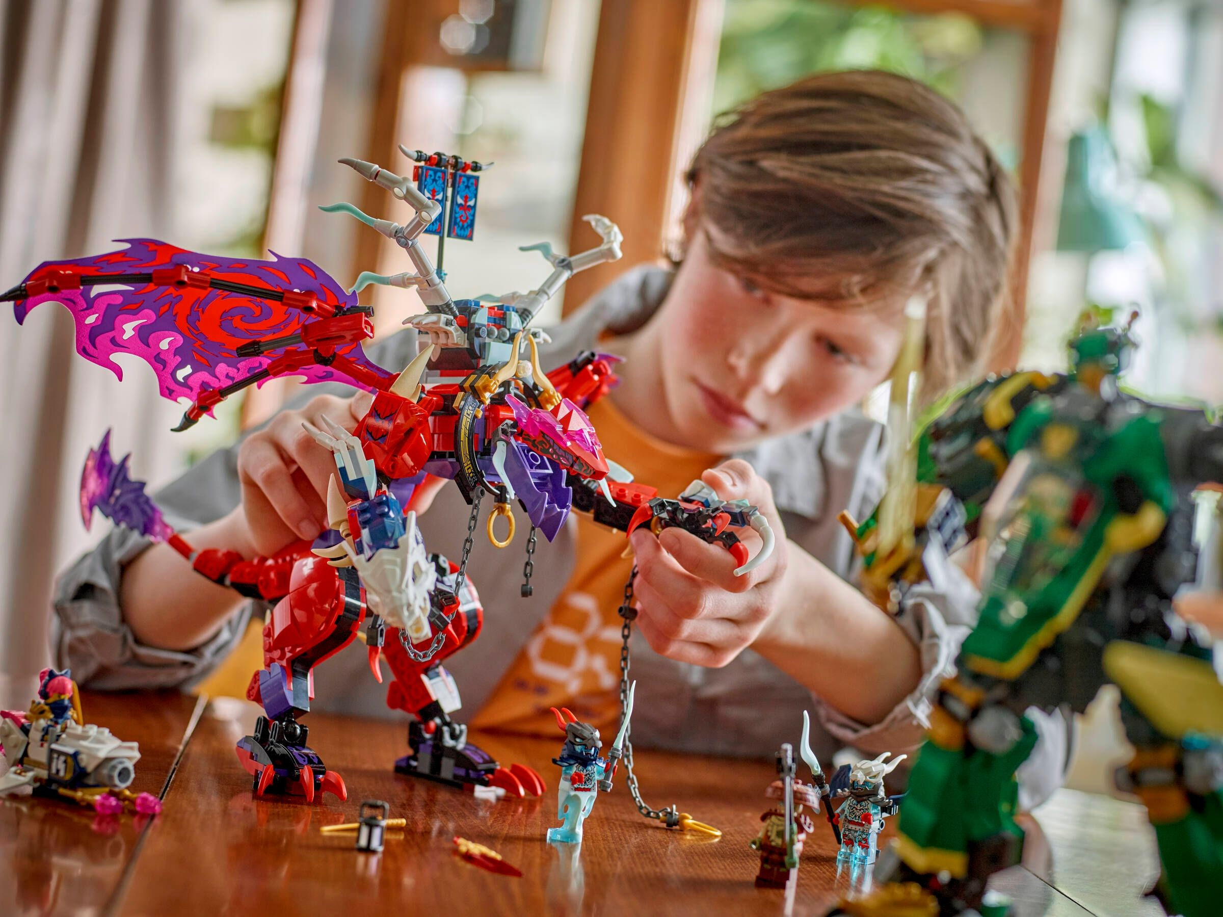Un ragazzo costruisce un drago LEGO rosso su un tavolo di legno con figure in miniatura.