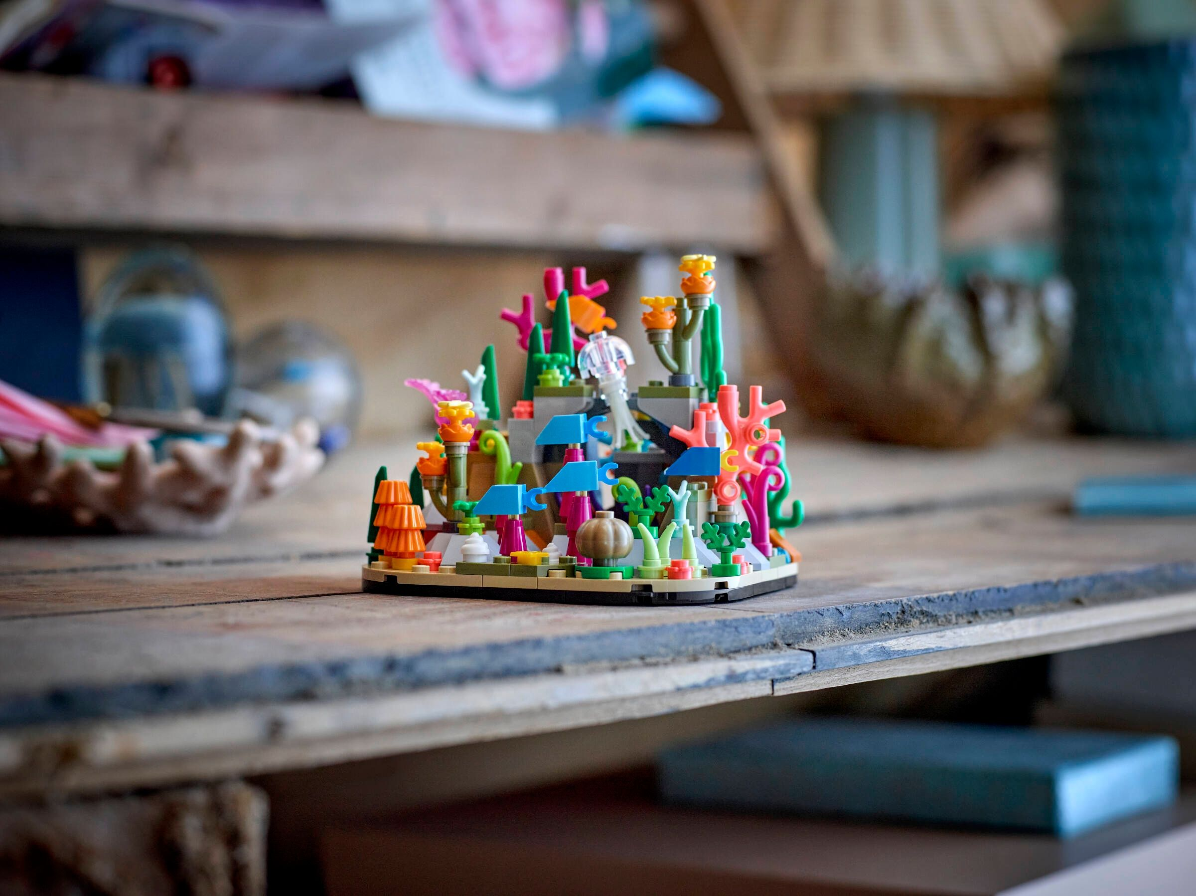 Ein kleines LEGO Korallenriff-Modell mit bunten Pflanzen und Meeresbewohnern steht auf einem Holzregal.