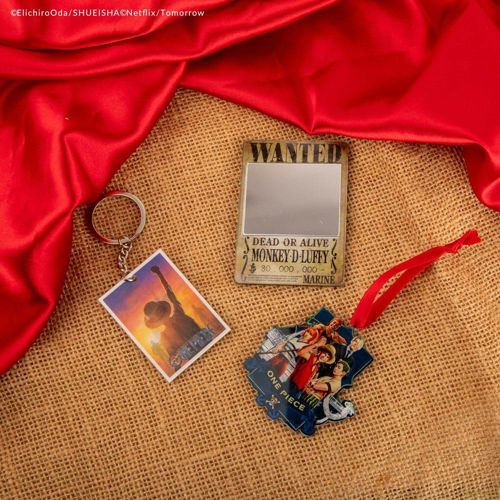 Merchandising de One Piece que incluye un llavero y póster sobre un fondo de tela roja.