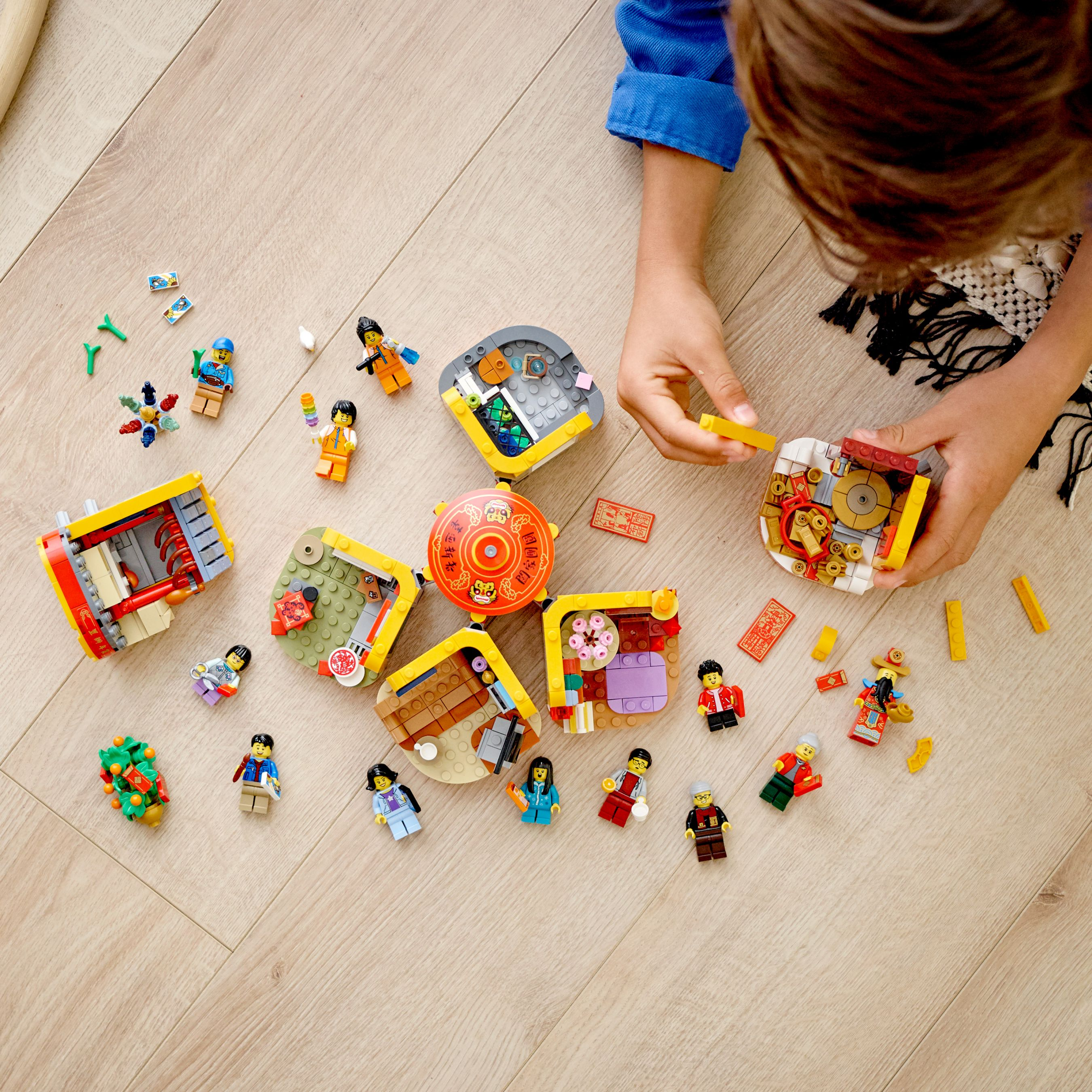 Un bambino costruisce insieme statuine e case Lego su un pavimento di legno.