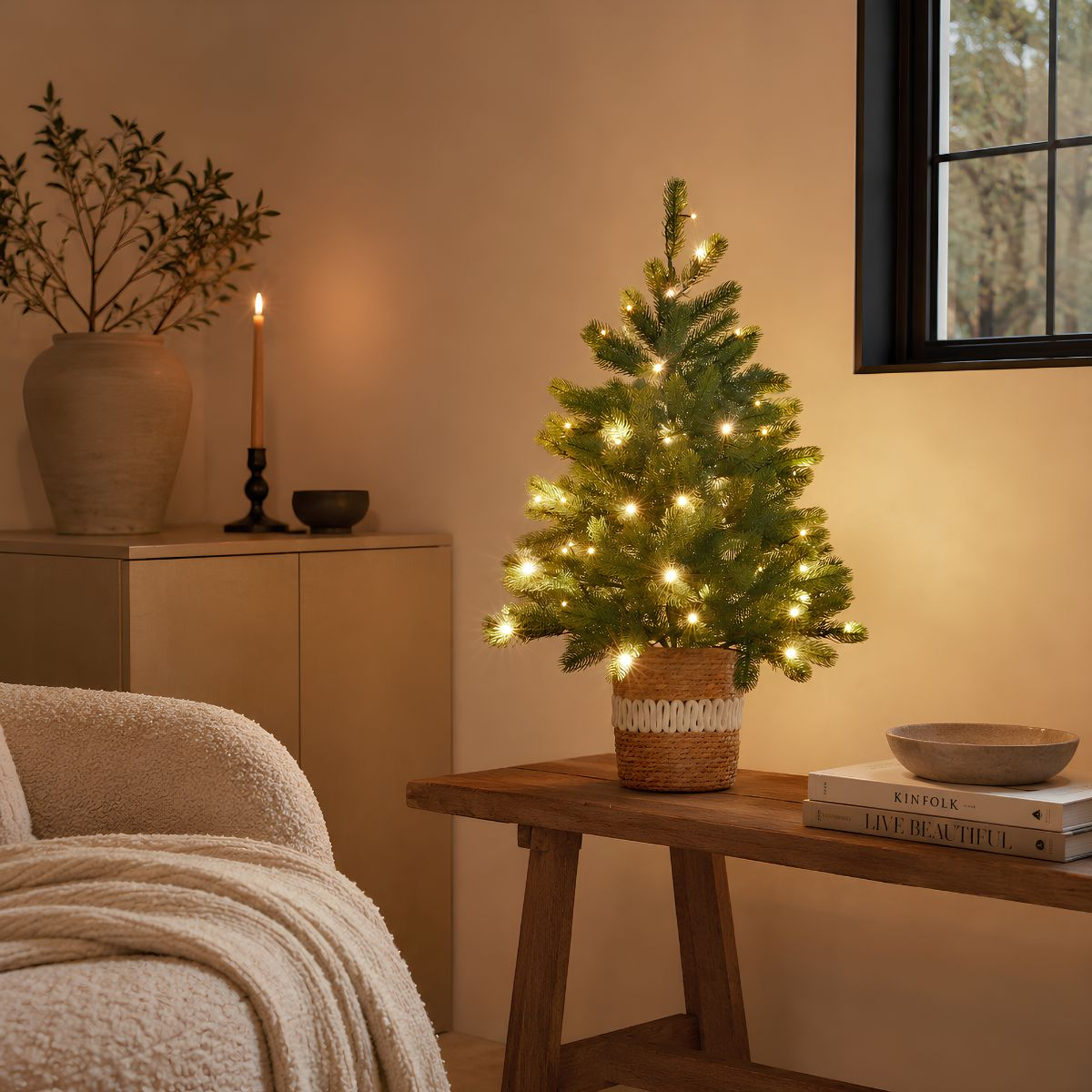 Small Christmas tree with string lights in a woven basket on a wooden bench in a cozy room.