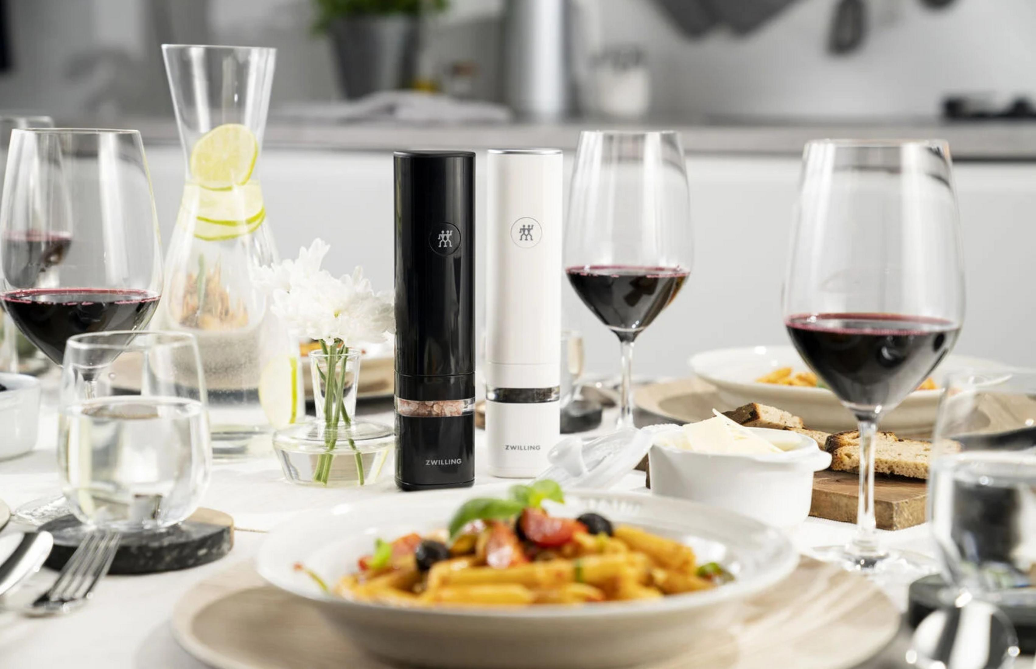 Tavola apparecchiata con pasta, vino, una caraffa e macinafuoco bianco e nera al centro.