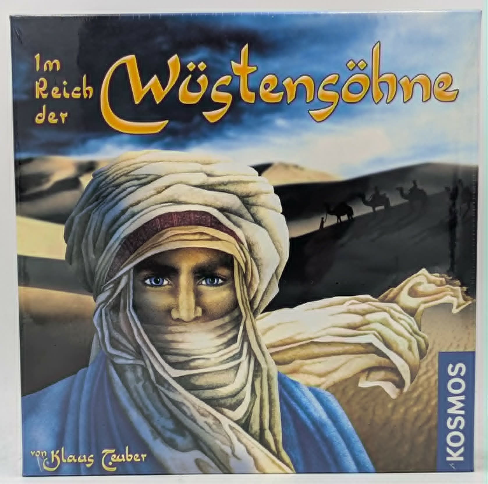 Brettspielschachtel mit einer Person im Turban in der Wüste und Kamelen im Hintergrund unter bewölktem Himmel.