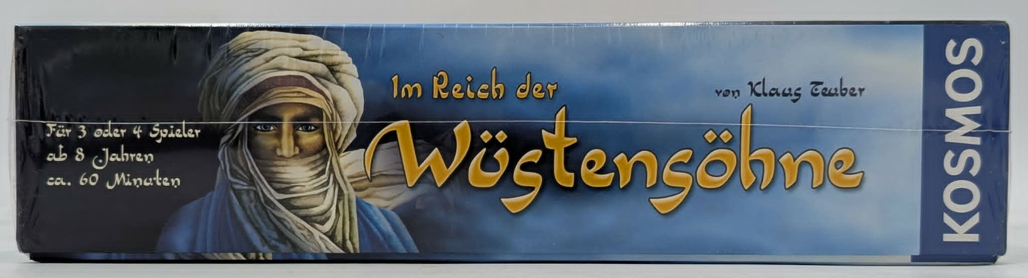 Seitenansicht einer Brettspielverpackung Im Reich der Wüstensöhne mit einer Person in traditioneller Kleidung.