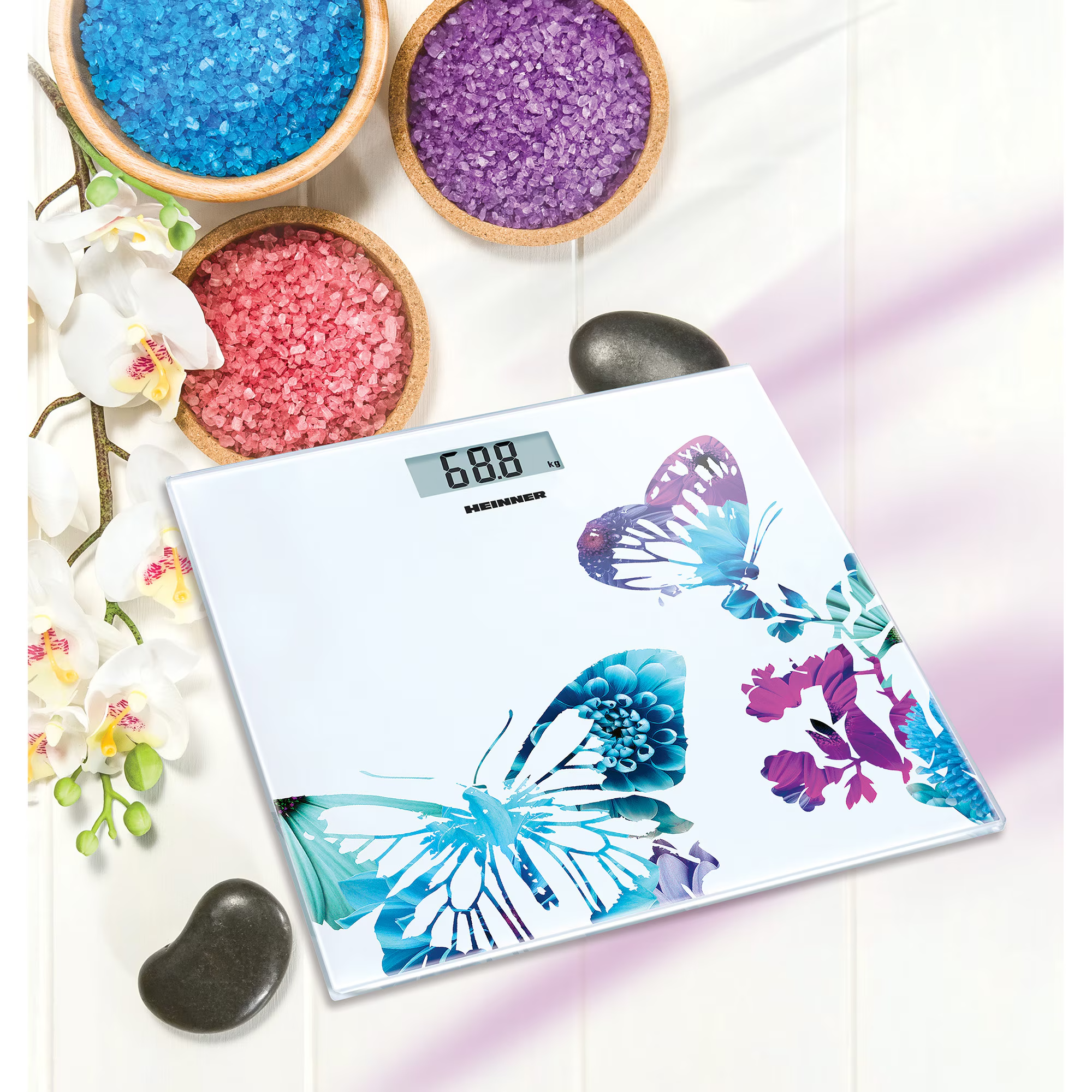 Pèse-personne numérique avec des papillons, entouré de sels de bain, de pierres et d'orchidées.