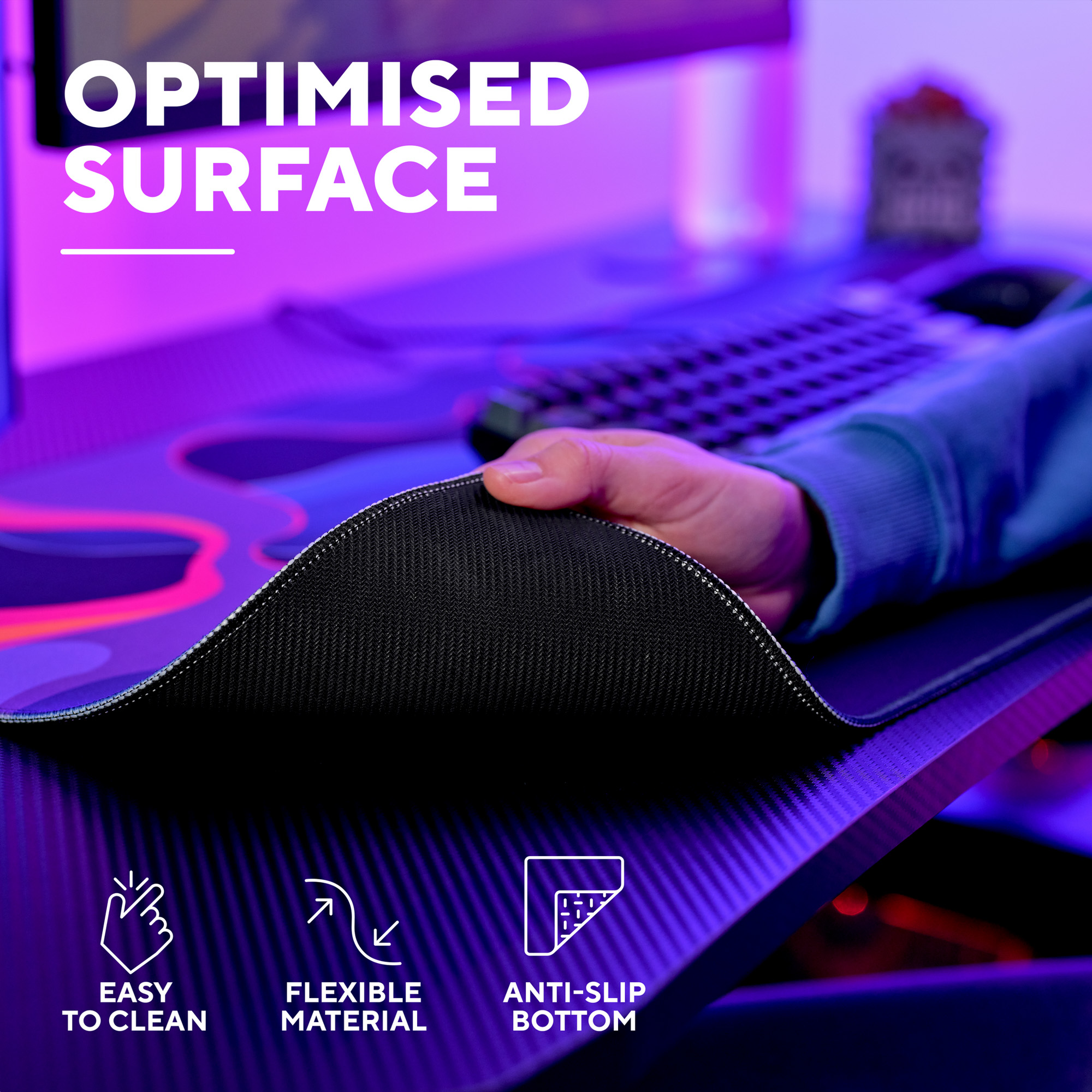 Hand hebt die rutschfeste Unterseite einer Gaming-Schreibtischunterlage, mit Tastatur und blauer Beleuchtung.