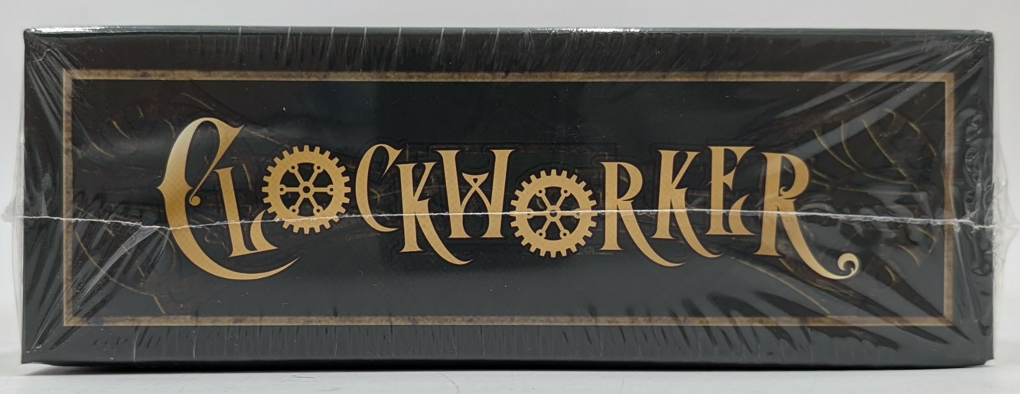 Das Wort "Clockworker" steht in goldenen Buchstaben mit Zahnrädern auf schwarzem Grund in Klarsichtfolie.