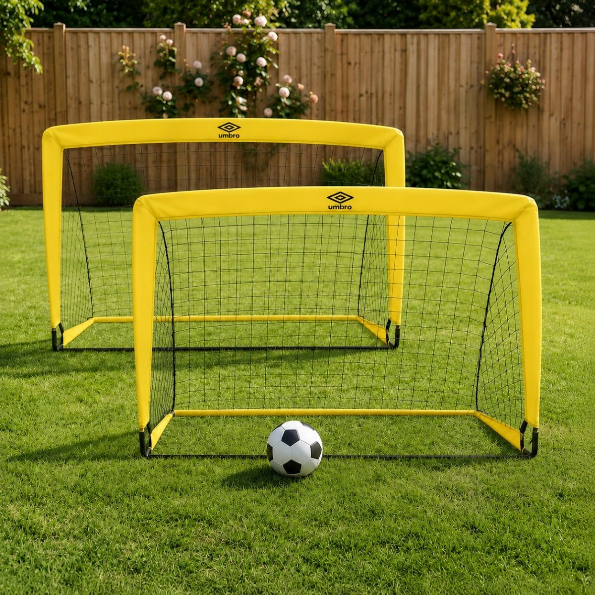 Zwei gelbe Umbro-Fußballtore auf grünem Rasen mit einem Ball vorne.