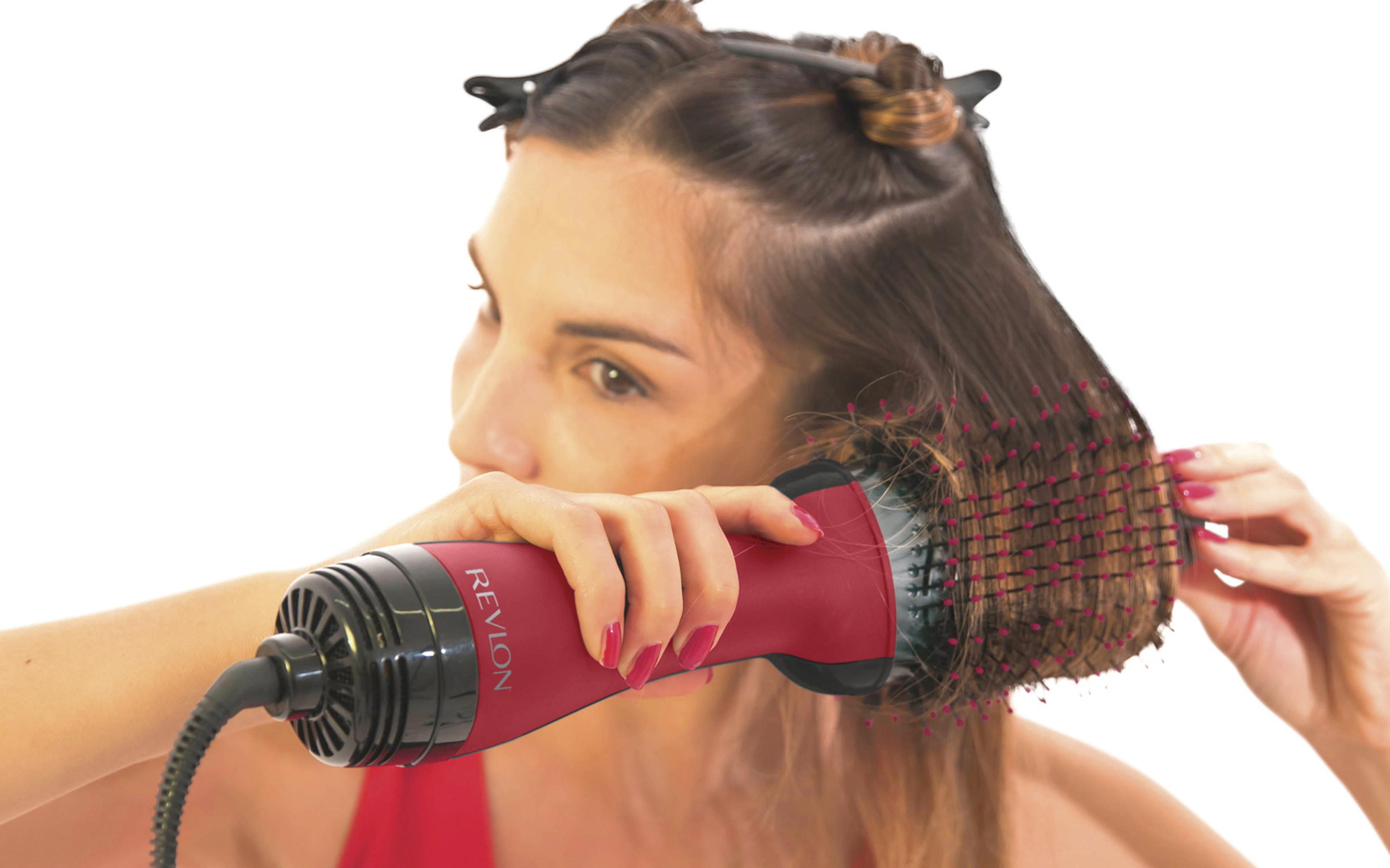 Una donna modella i suoi capelli castani con una spazzola asciugacapelli Revlon rossa.