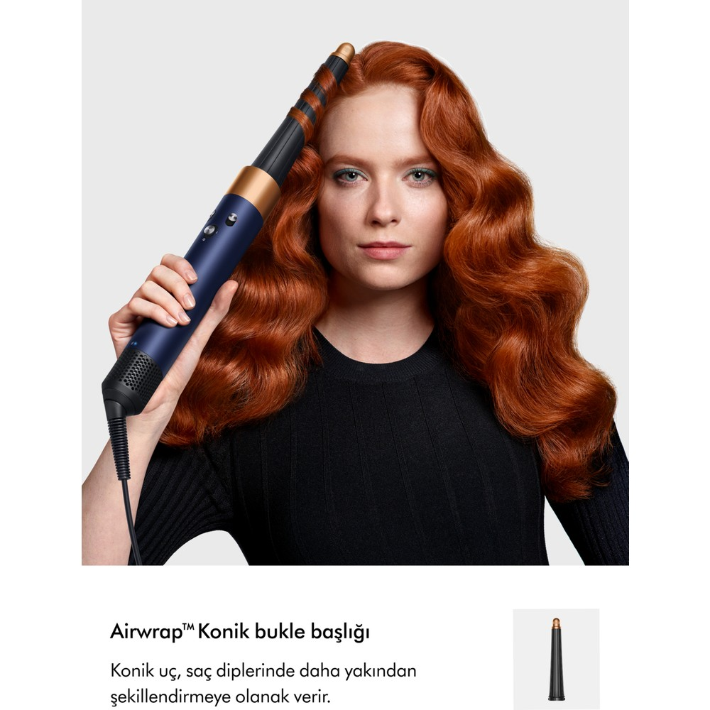 Una donna con capelli rossi ondulati tiene uno styler Airwrap blu su sfondo grigio.