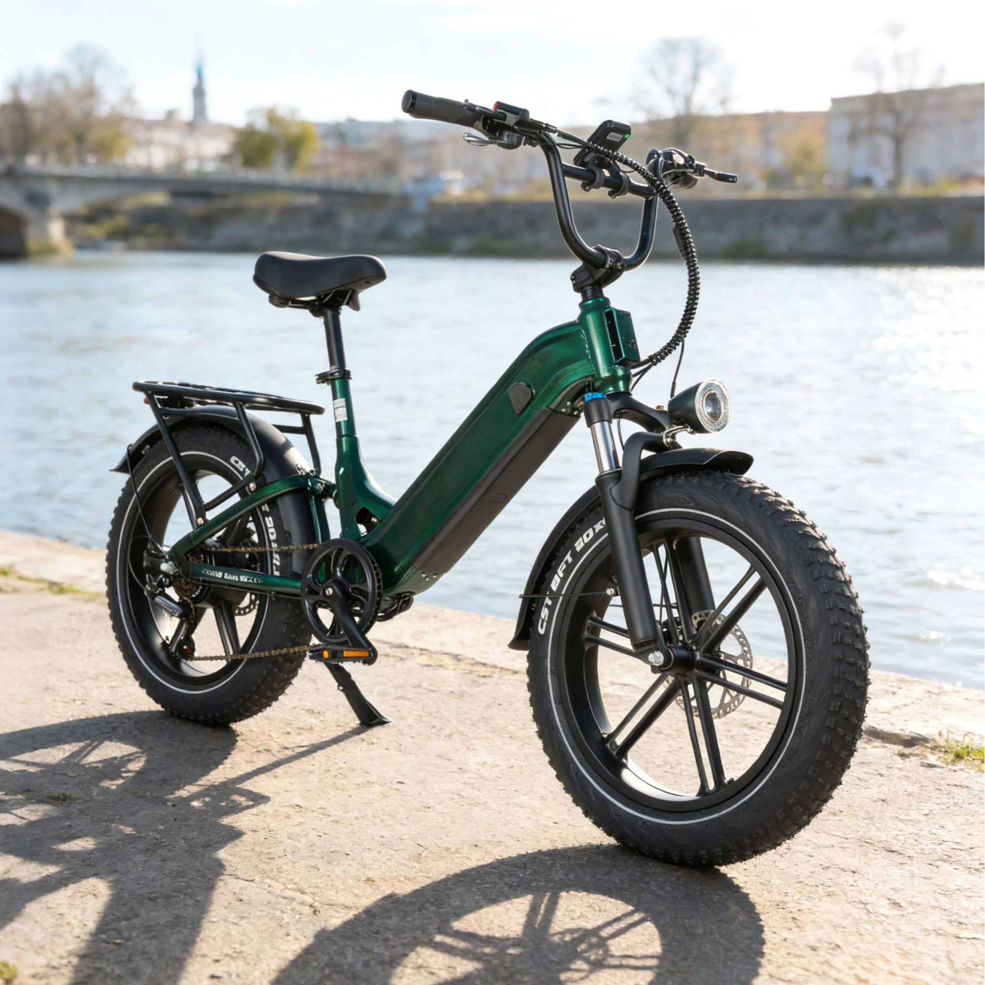 Zielony rower elektryczny z grubymi oponami stoi nad brzegiem rzeki na tle rozmytego pejzażu miasta.