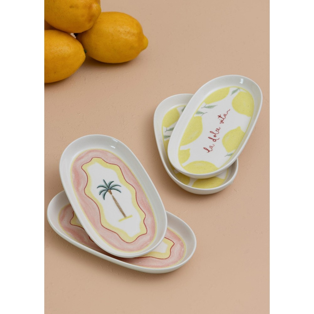 Bej arka plan üzerinde palmiye ve limon desenli dört oval seramik tabak, gerçek limonların yanında.