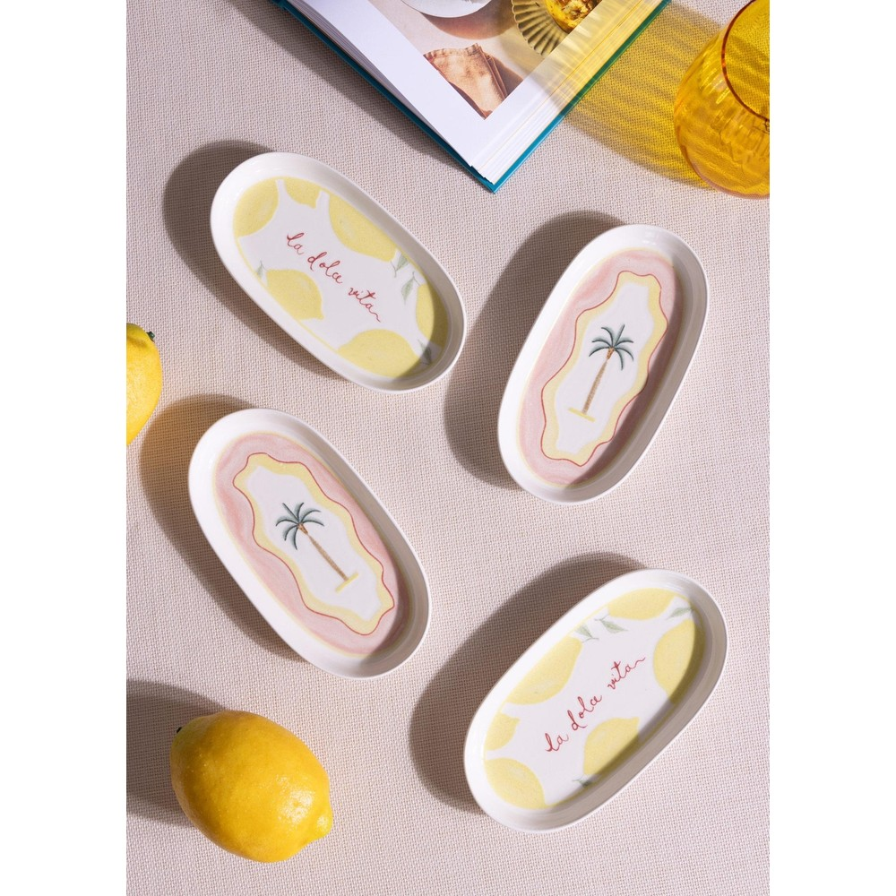Bej kumaş üzerinde limon ve palmiye motifli dört oval seramik tabak, iki tam limon ve bir dergi.