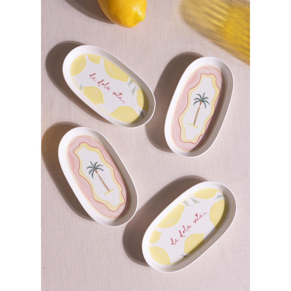 Dokulu bej yüzey üzerinde limon ve palmiye desenli dört oval seramik tabak ve bütün bir limon.