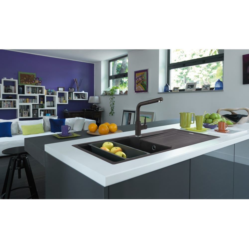 Un'isola cucina moderna con lavello scuro, rubinetto e mele verdi, in una stanza luminosa con parete viola.