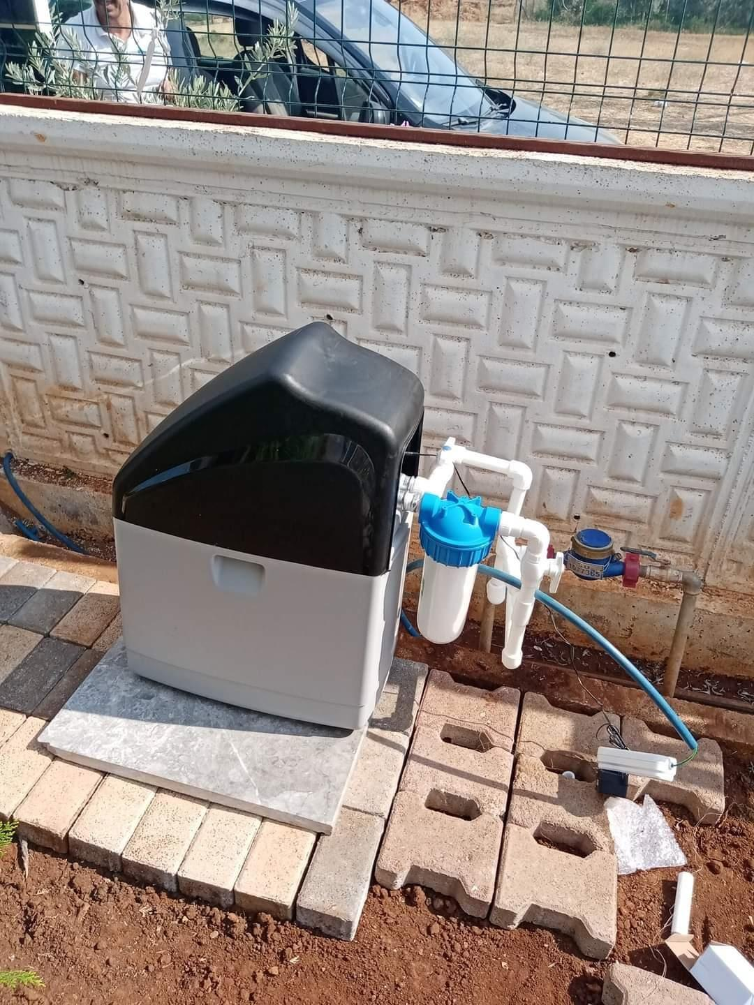 Gri tabanlı ve siyah kapaklı bir su yumuşatma sistemi dışarıda taş parke üzerinde duruyor.