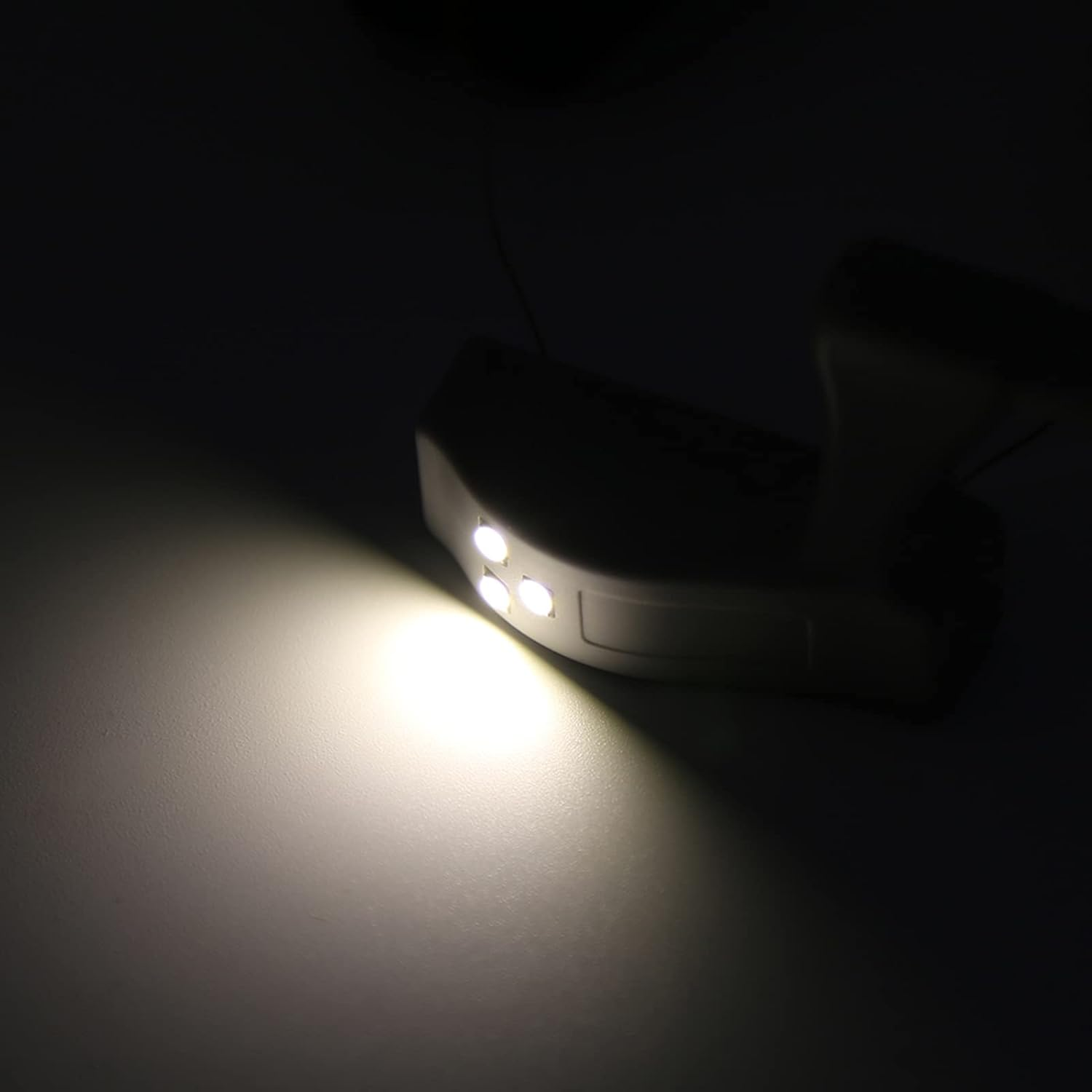 Ein kleines weißes elektronisches Gerät mit drei LEDs projiziert einen hellen Strahl auf eine dunkle Oberfläche.